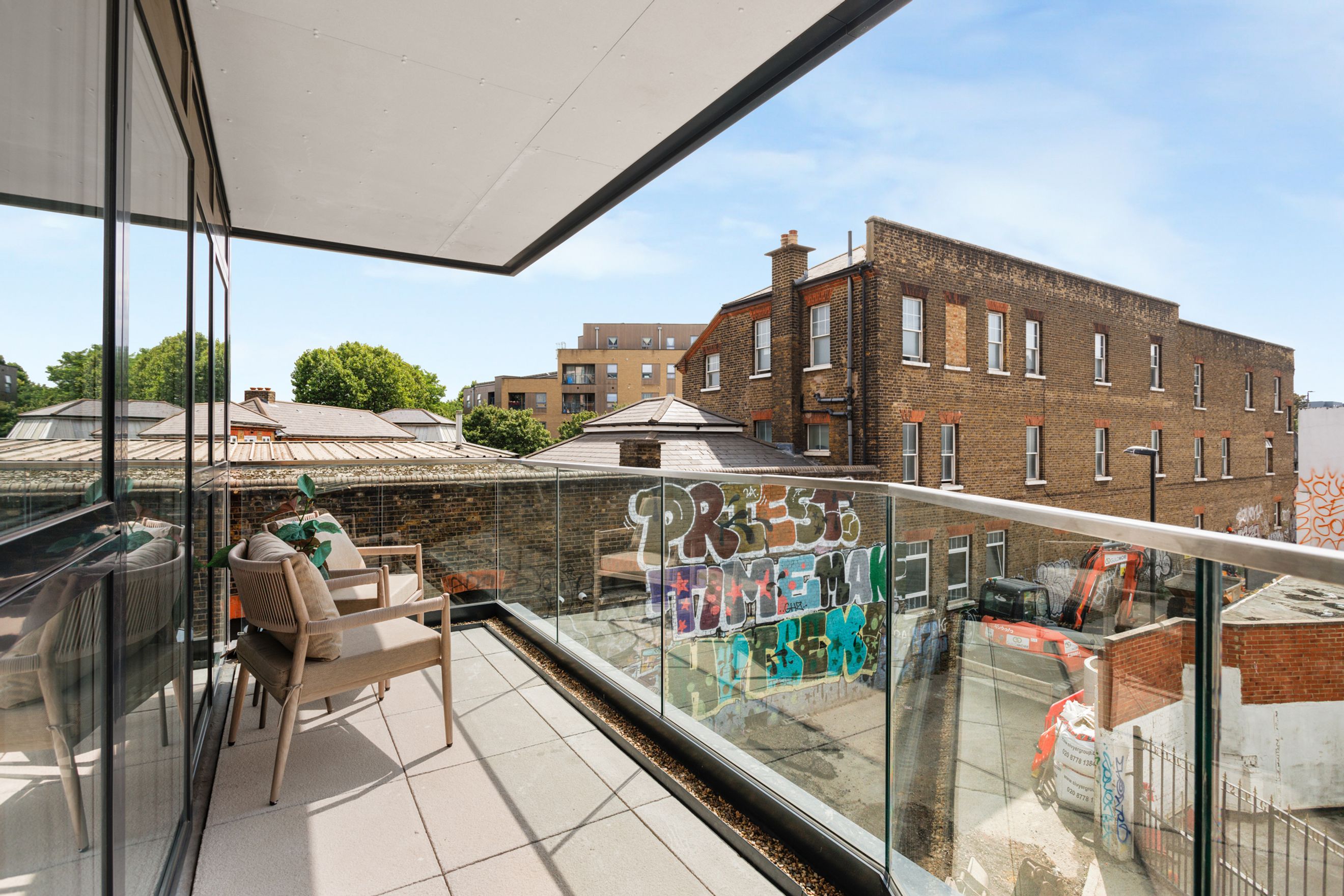 A balcony with two chairs and a glass railing overlooking a cityscape with graffiti.