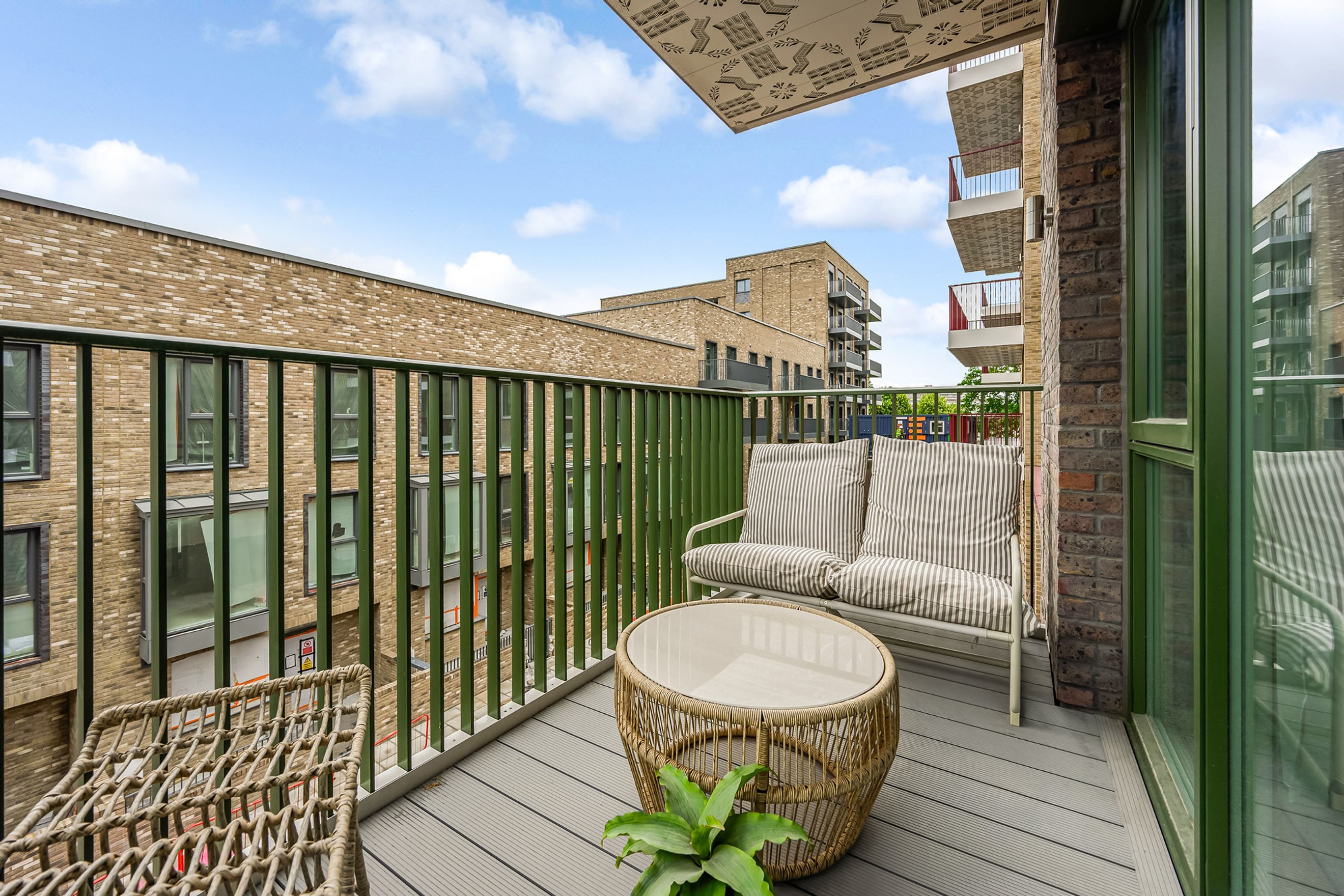 A balcony with a sofa, coffee table, and chair overlooking apartment buildings.