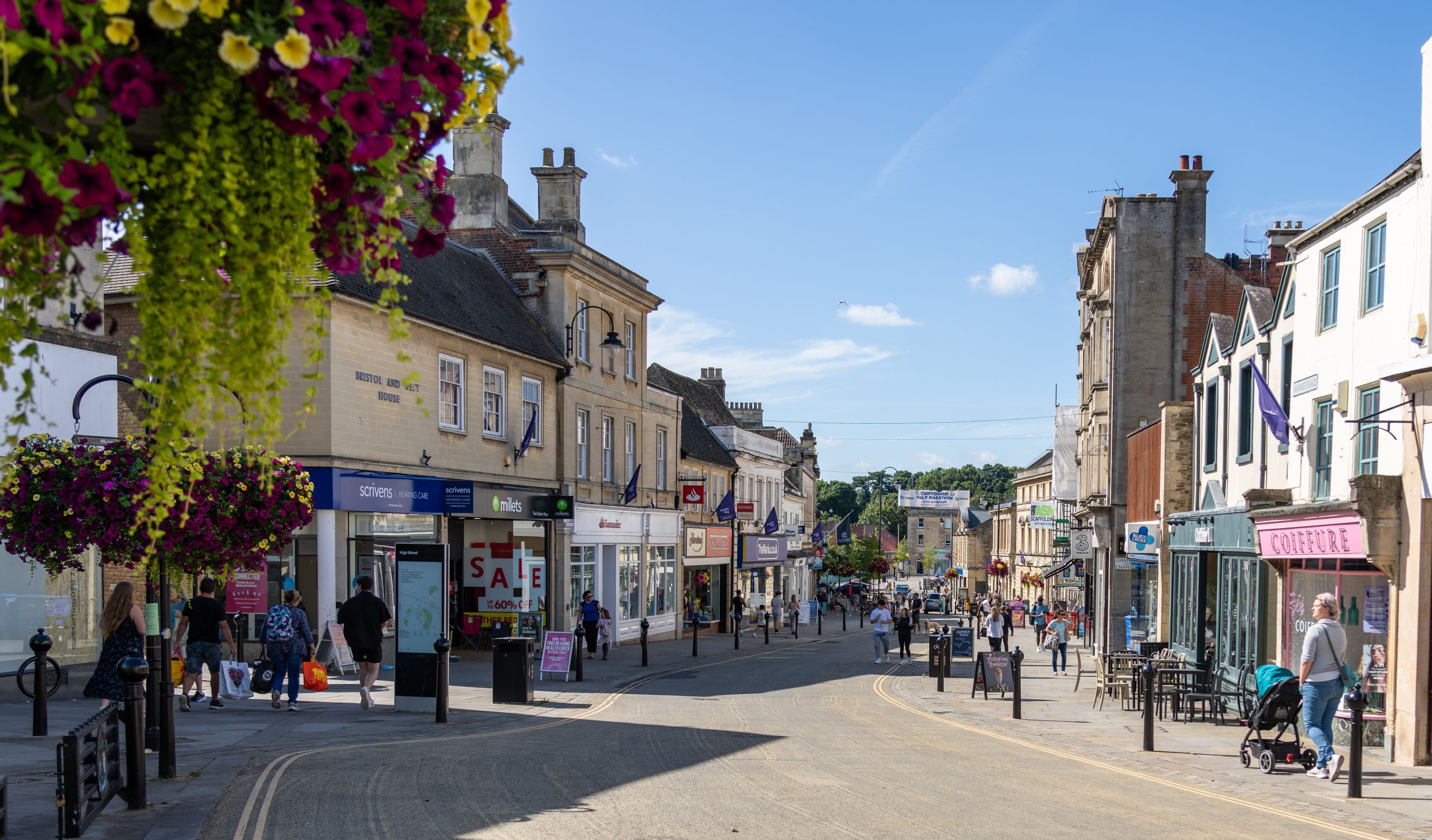 A bustling high street lined with shops and pedestrians on a sunny day.