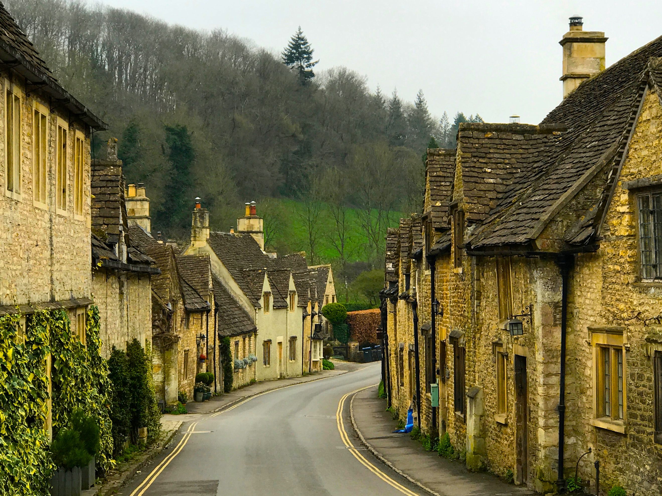 A winding road lined with stone cottages and trees on a hill.