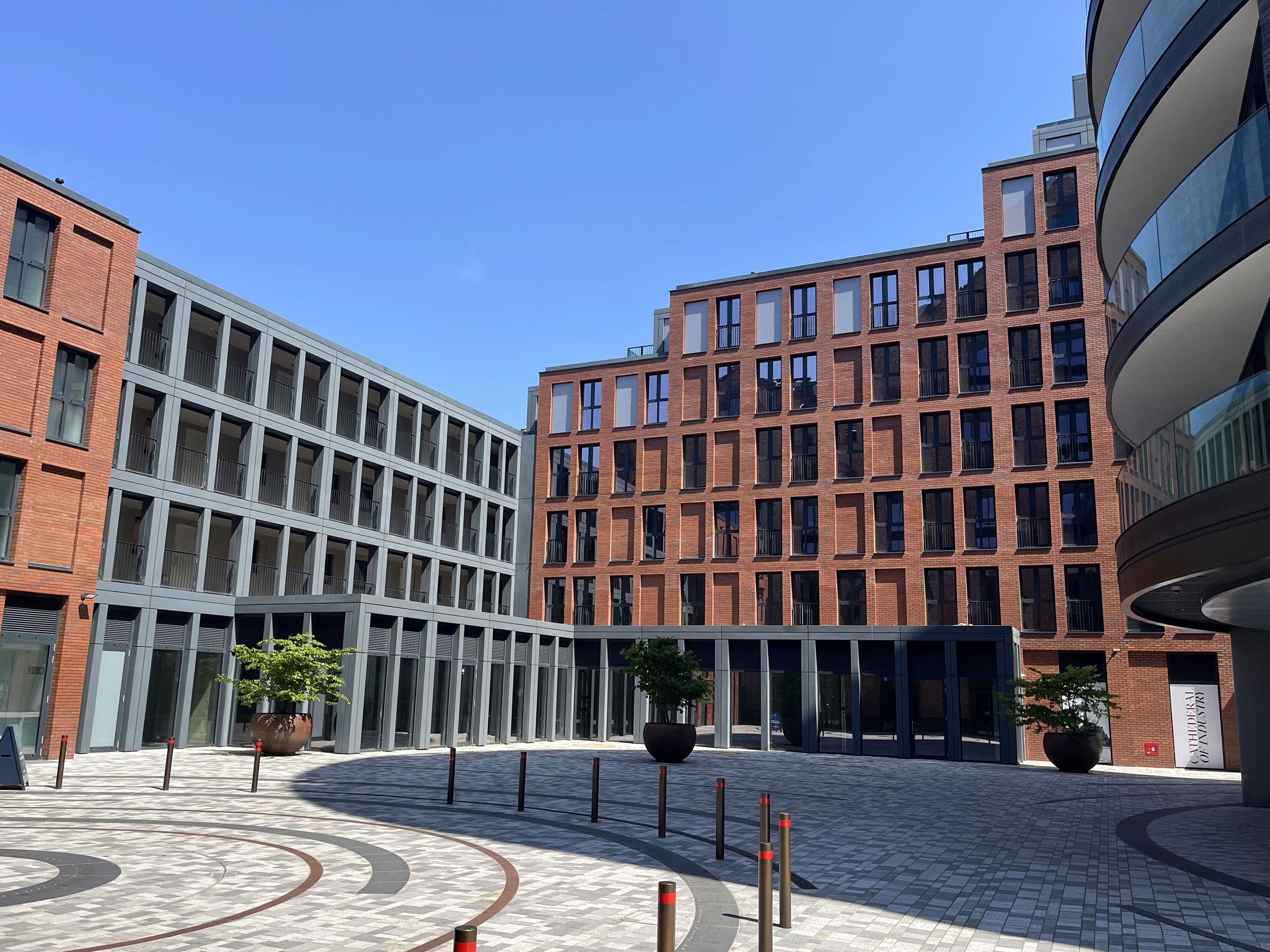 A courtyard surrounded by modern brick and grey buildings with balconies and large windows.