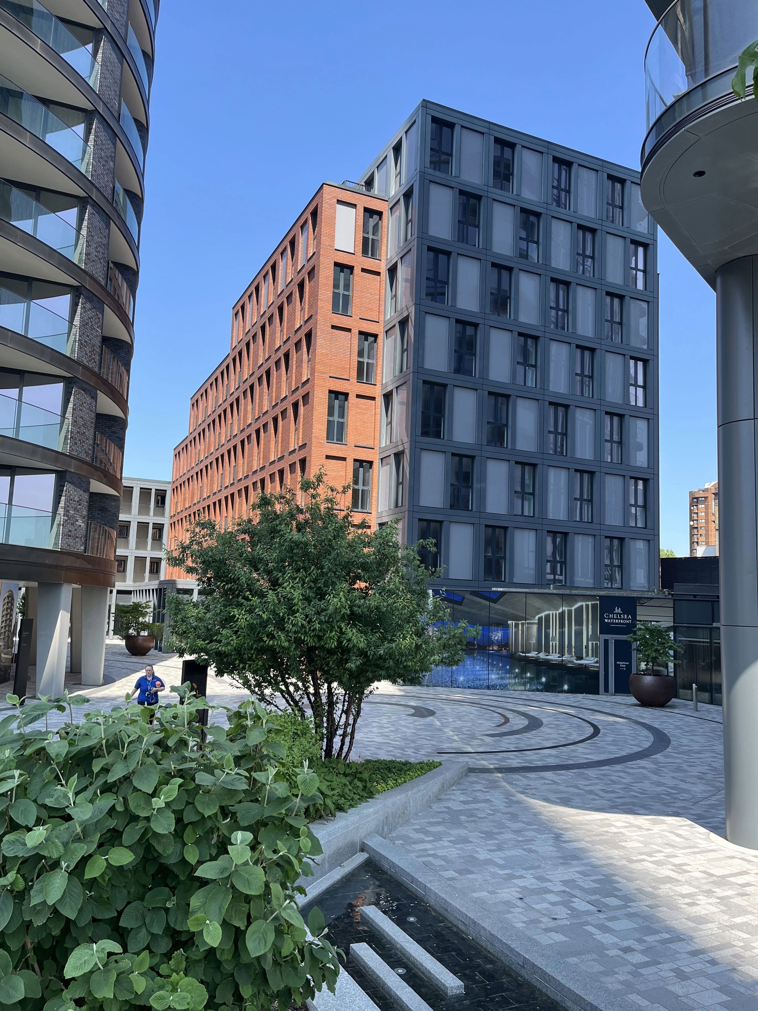 A courtyard with modern buildings, a tree, and a person walking.