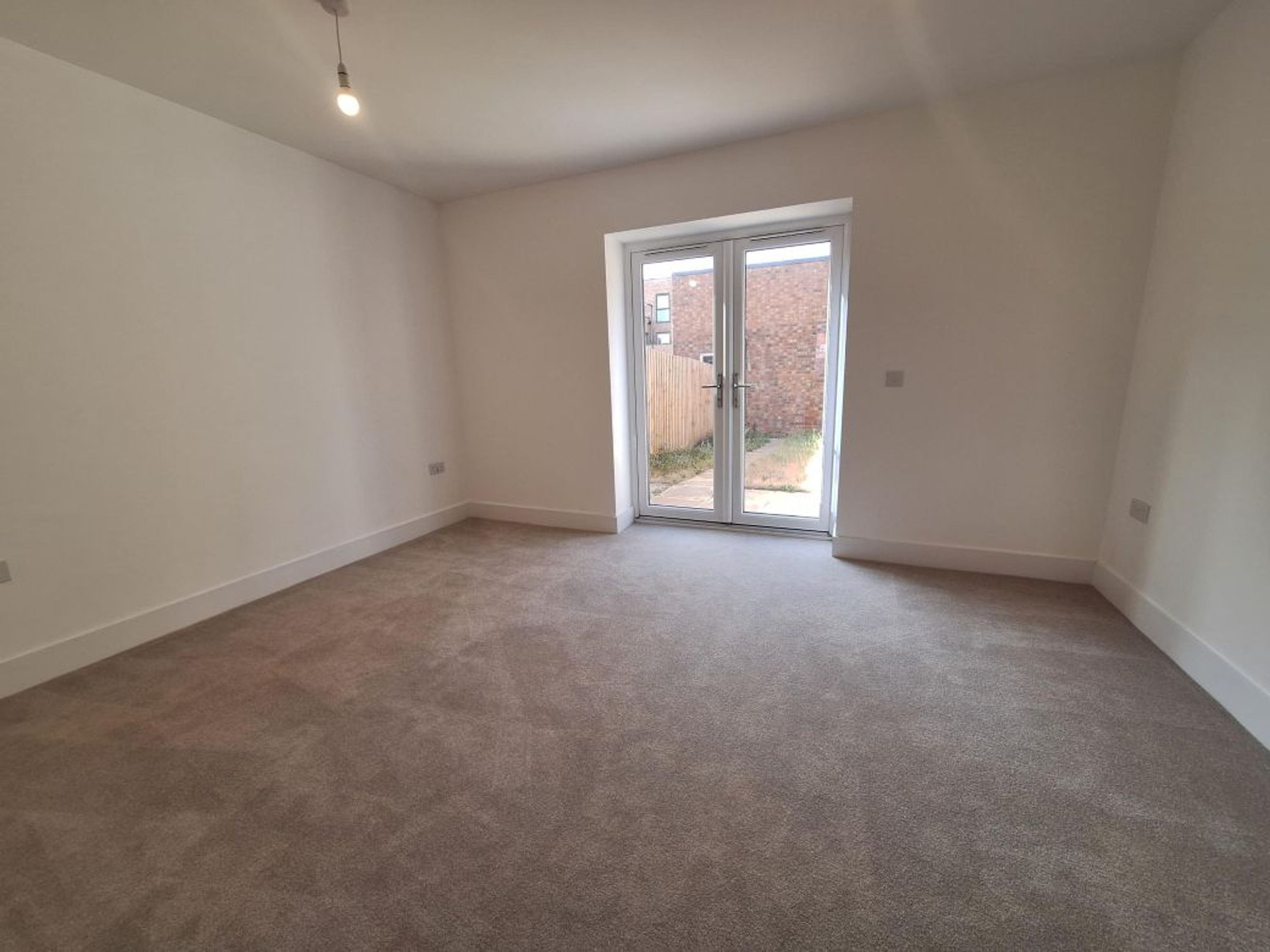 A room with grey carpet and double glass doors.