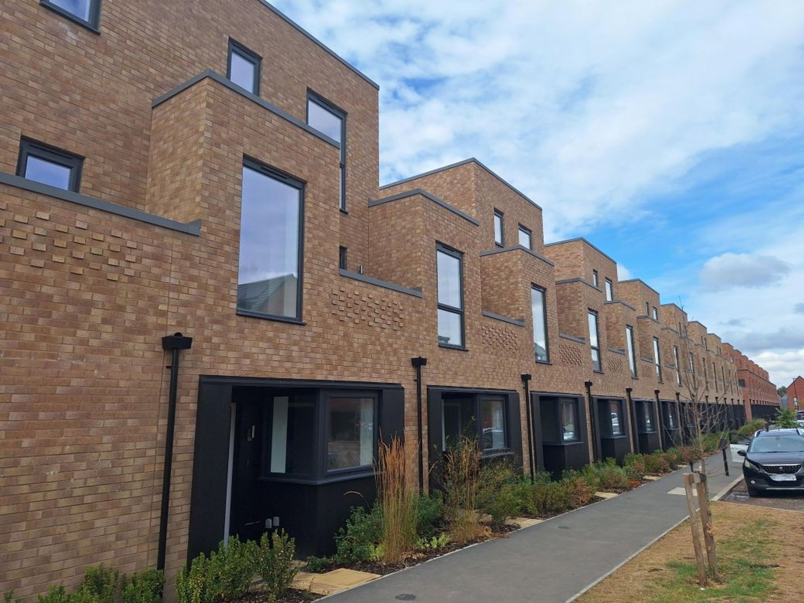 A row of modern brick townhouses with large windows and dark trim under a cloudy sky.
