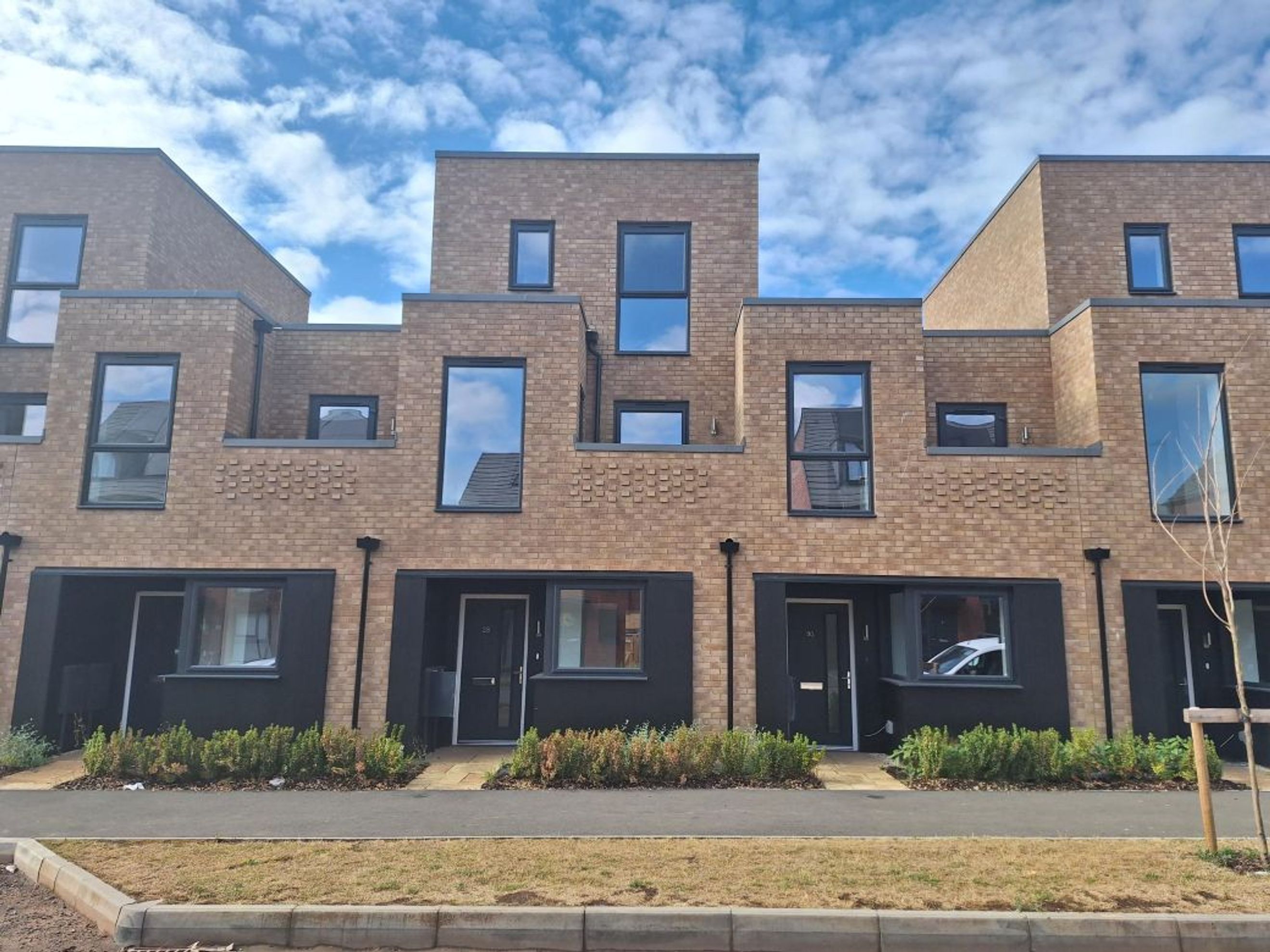 A row of modern brick townhouses with black lower levels and large windows under a cloudy sky.