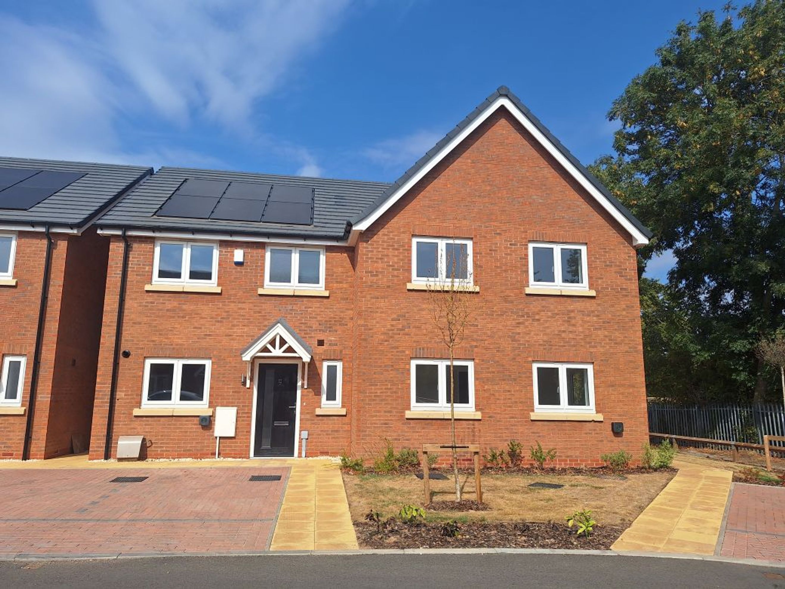 A modern red brick house with white-framed windows and a grey roof with solar panels.