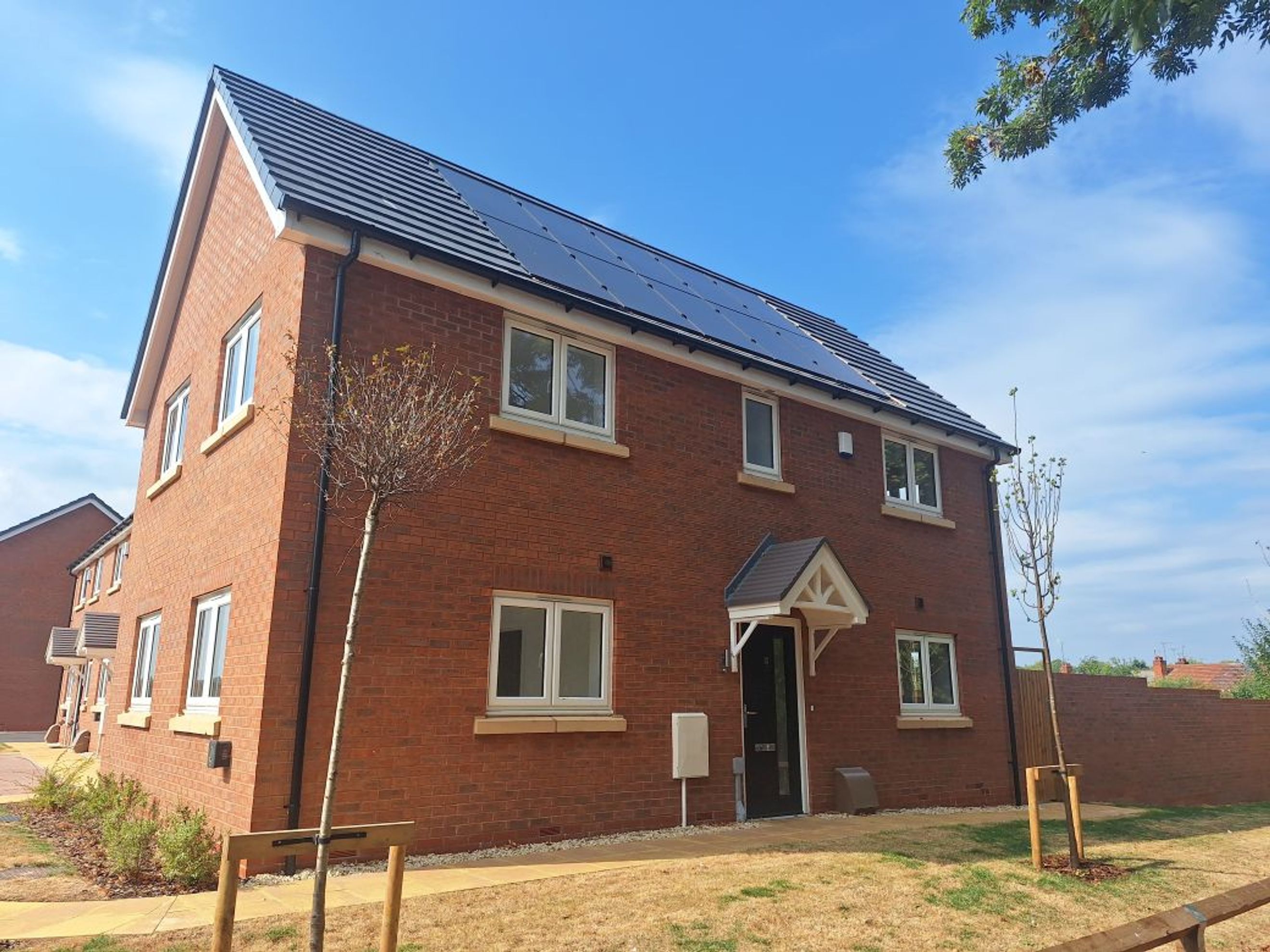 A modern brick house with solar panels on the roof and white-framed windows.