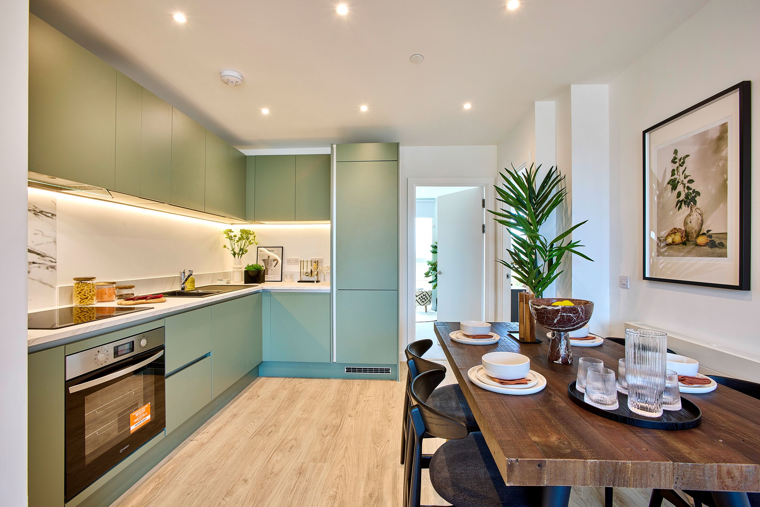 A kitchen and dining area with sage-green cabinets, a wooden dining table, and place settings.
