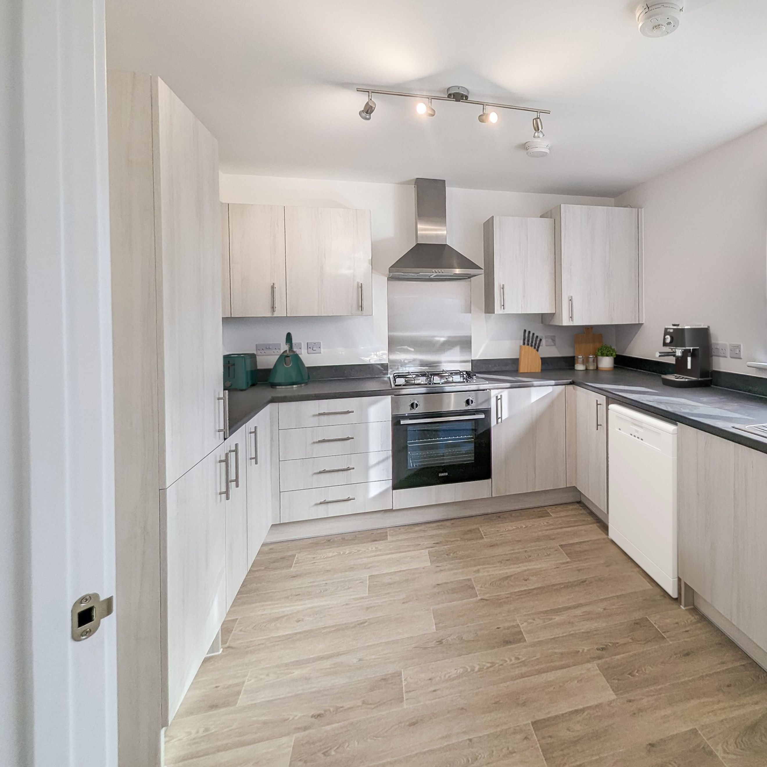A modern kitchen with light wood cabinets, a gas stove, and a dishwasher.