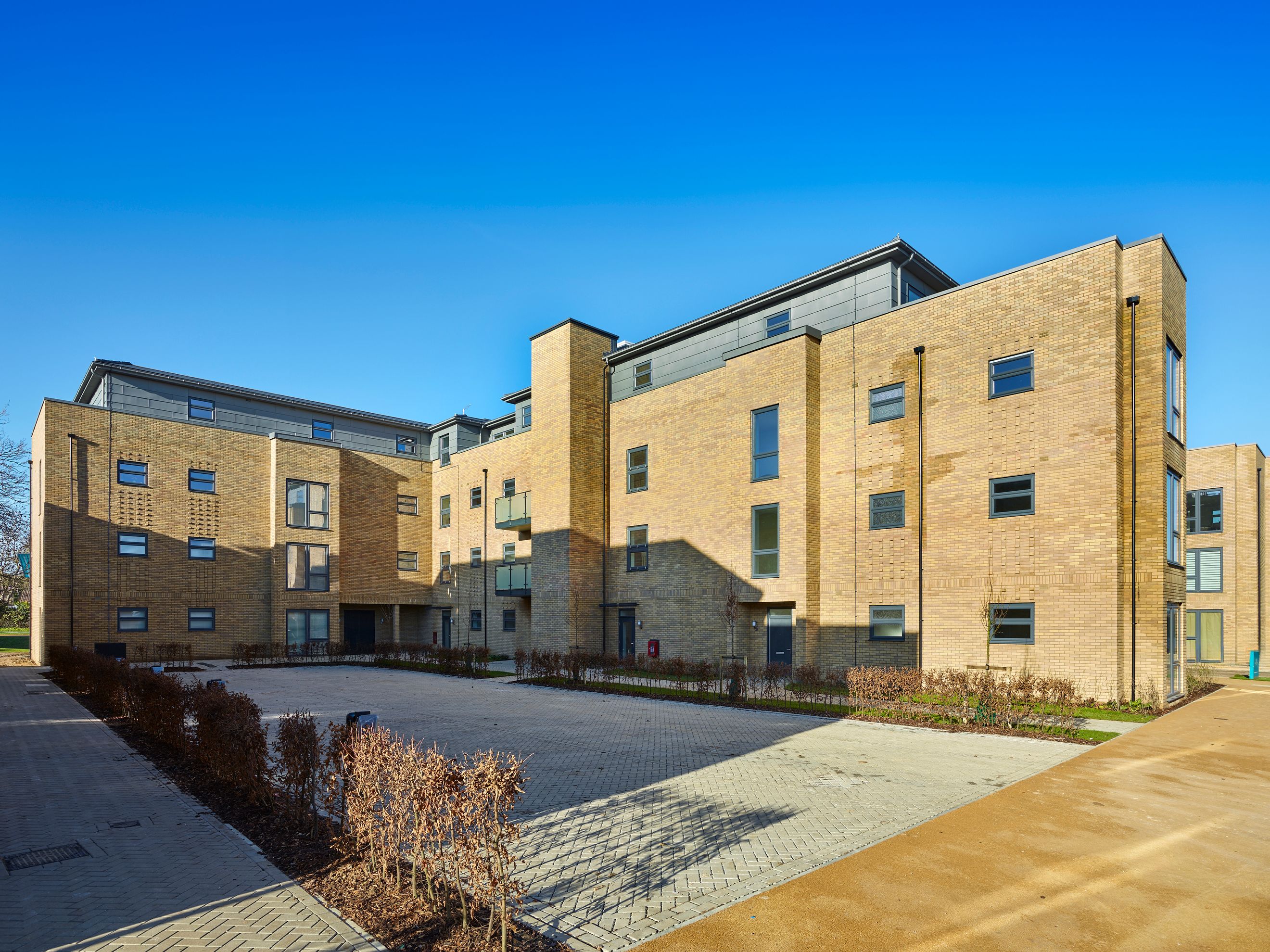 A modern apartment building with brick exterior and balconies under a clear blue sky.