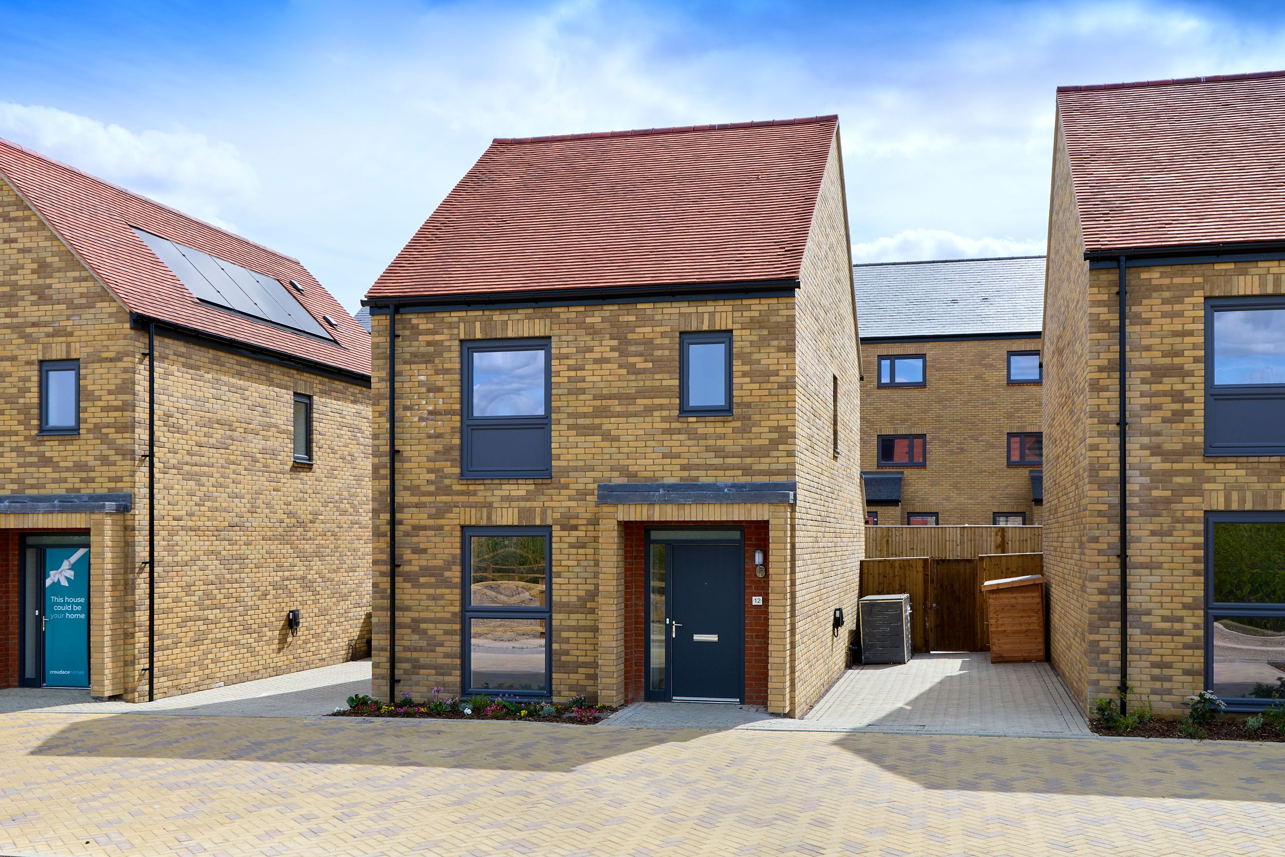 A row of modern brick houses with red tiled roofs and dark windows under a blue sky.