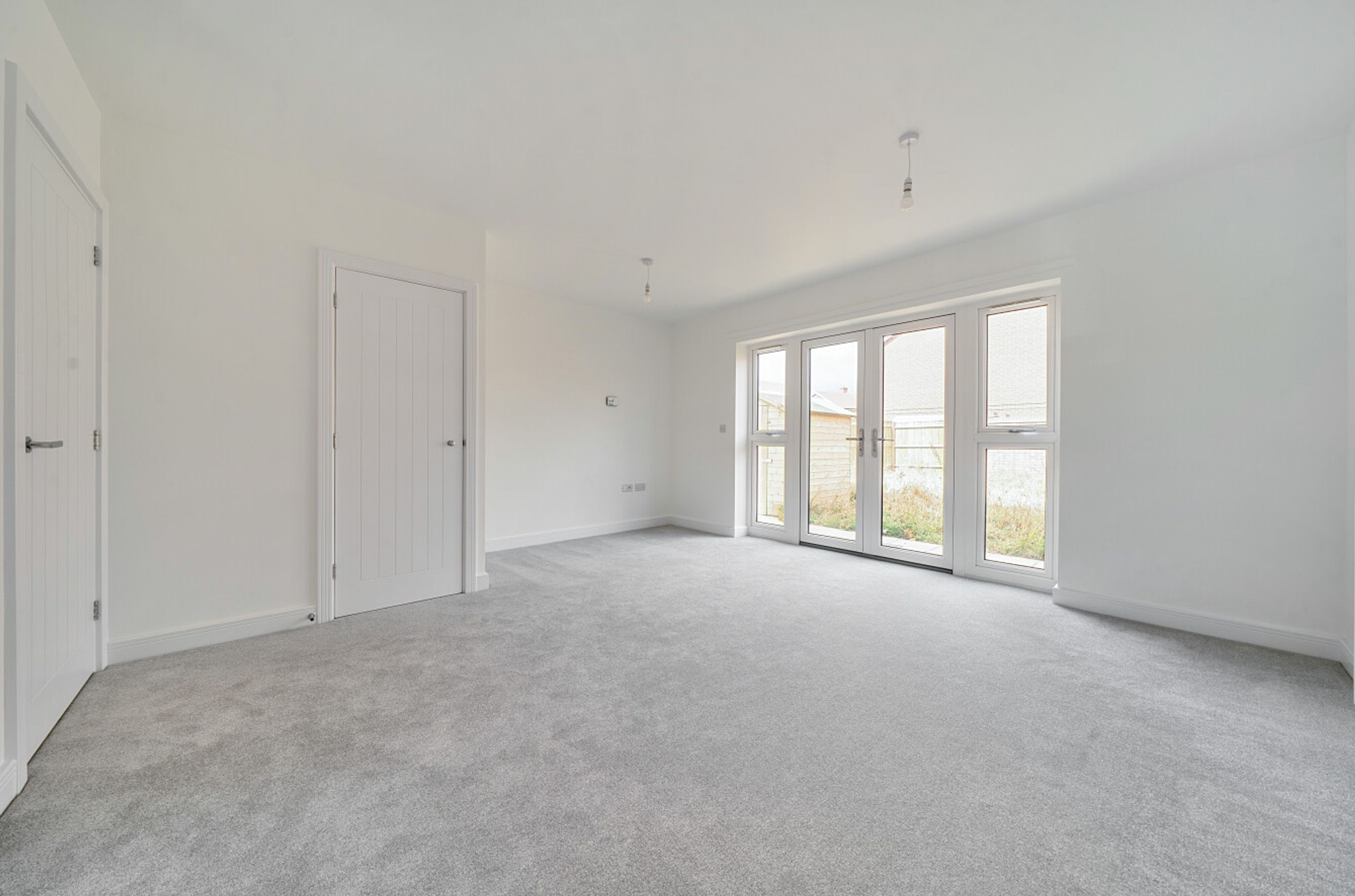 A room with two doors and double glass doors leading outside, with grey carpet and white walls.