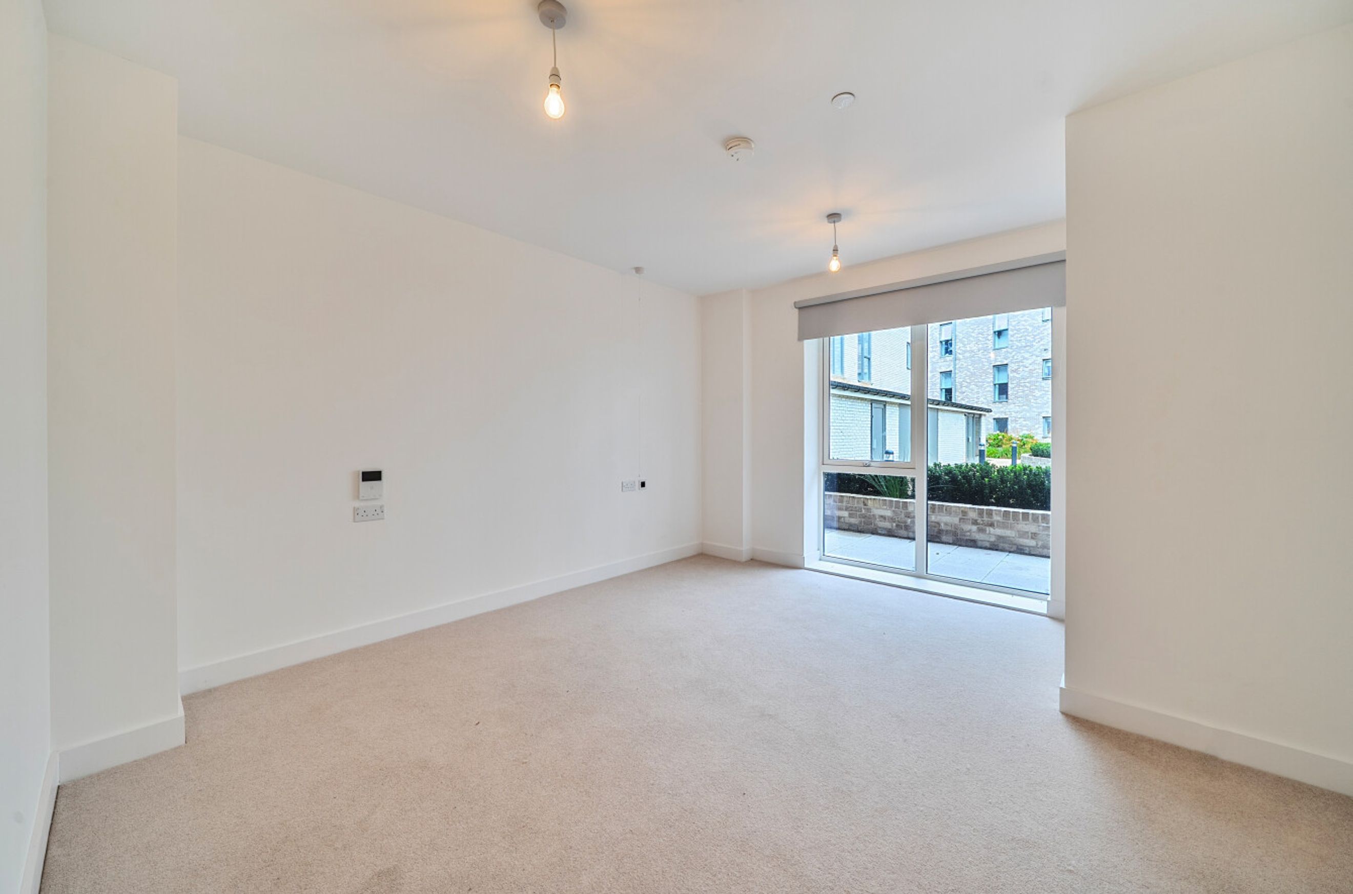 A spacious, empty room with beige carpet and a large window overlooking an exterior view.