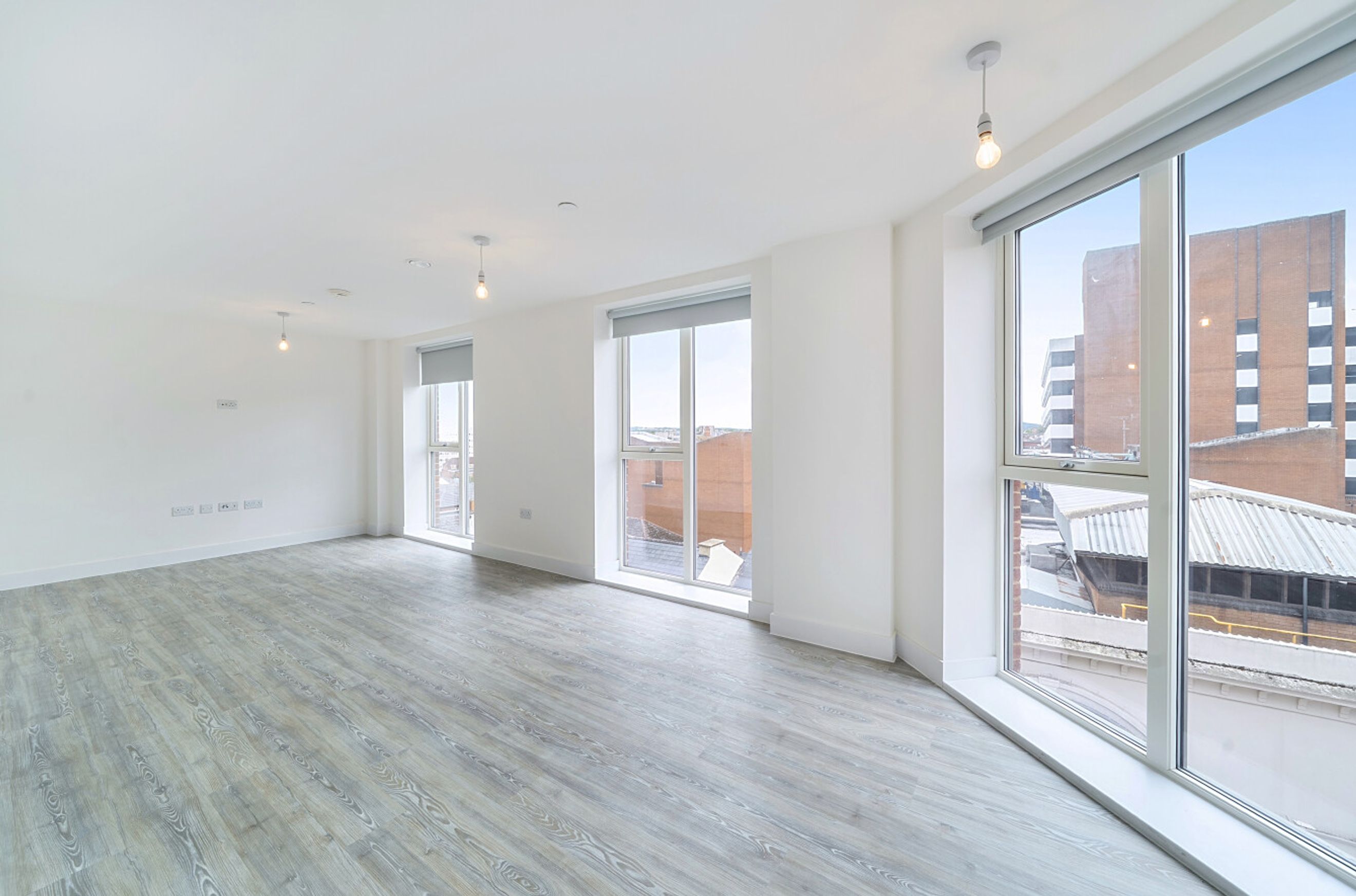 A spacious, empty room with large windows and light wood-effect flooring.