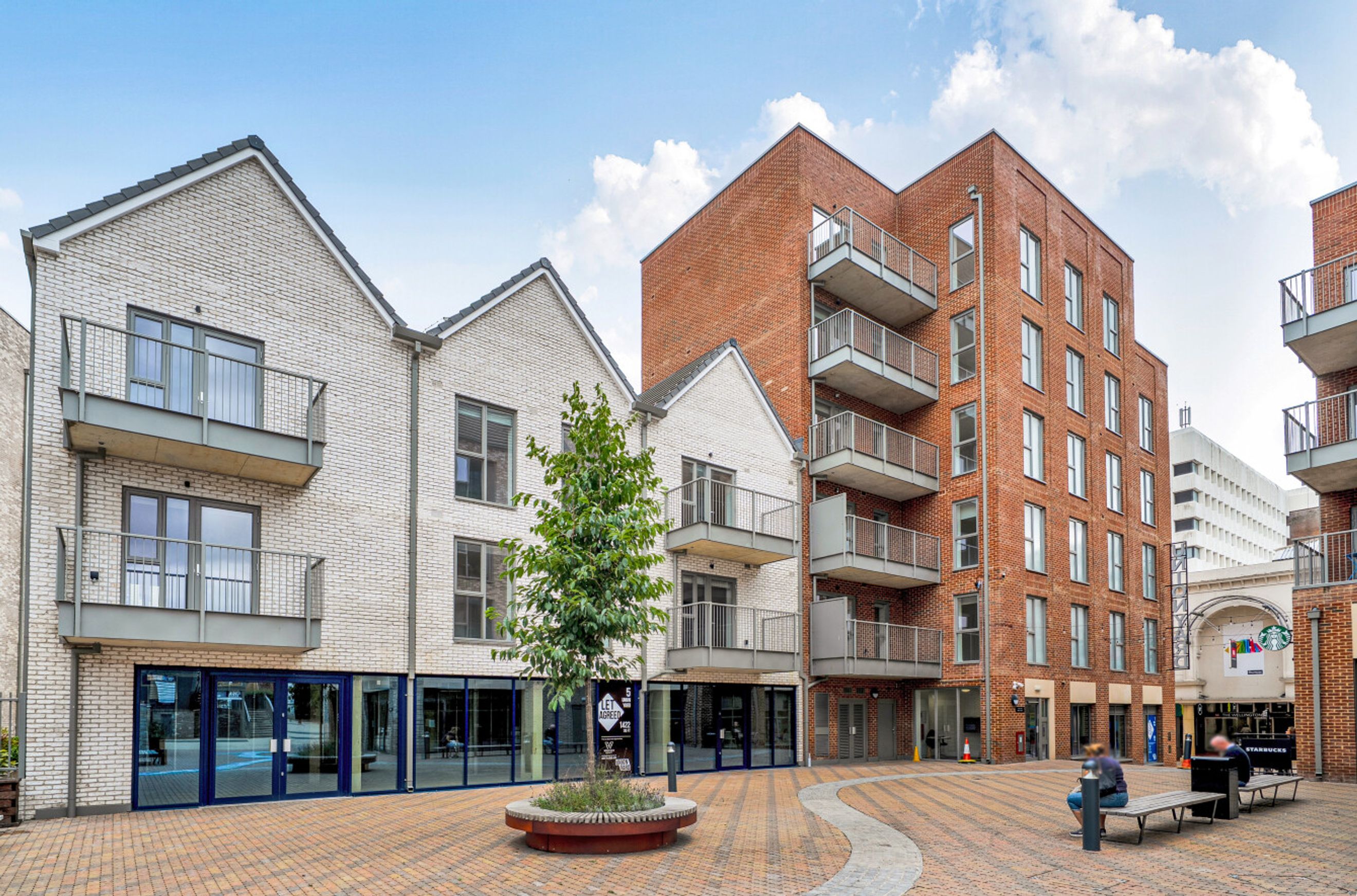 A modern building complex with brick and white facades, balconies, and ground-floor commercial spaces.