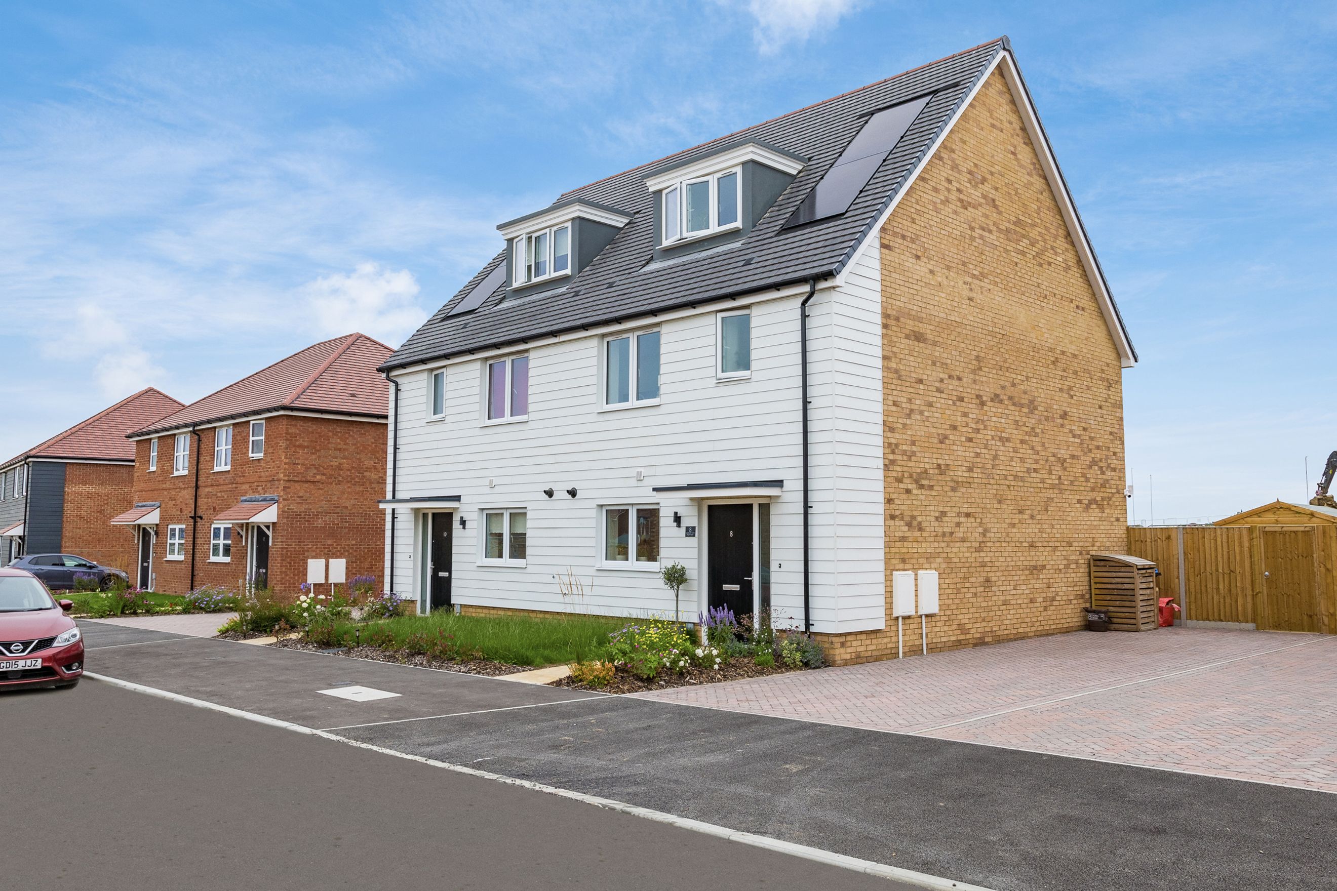 A modern semi-detached house with white cladding and brick exterior, solar panels, and a paved driveway.