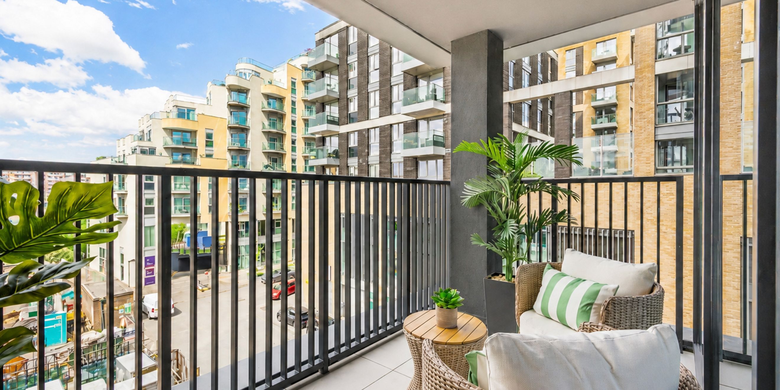 A balcony with wicker furniture, plants, and a view of apartment buildings.