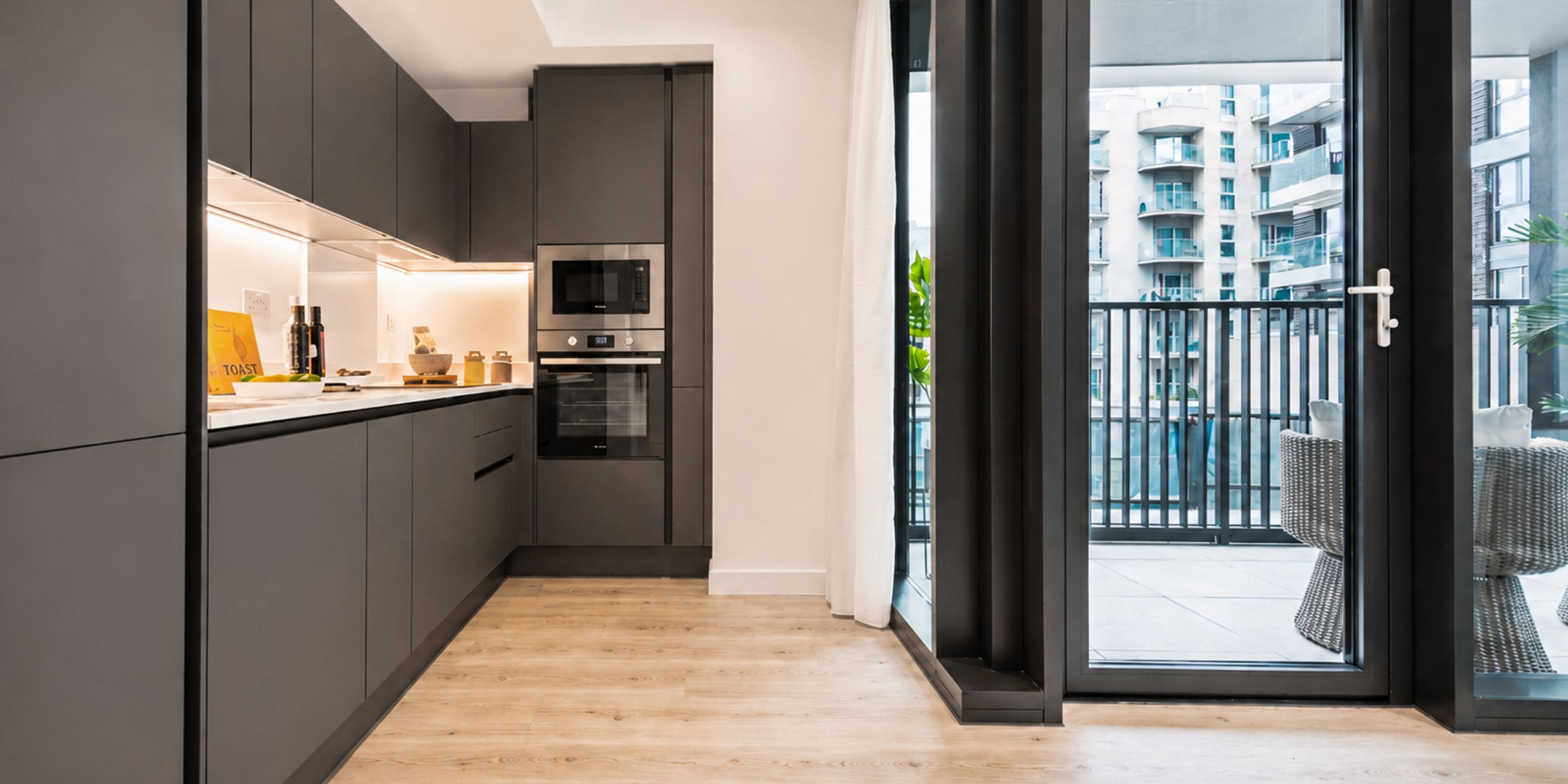 A modern kitchen with dark cabinets, integrated appliances, and a balcony view.