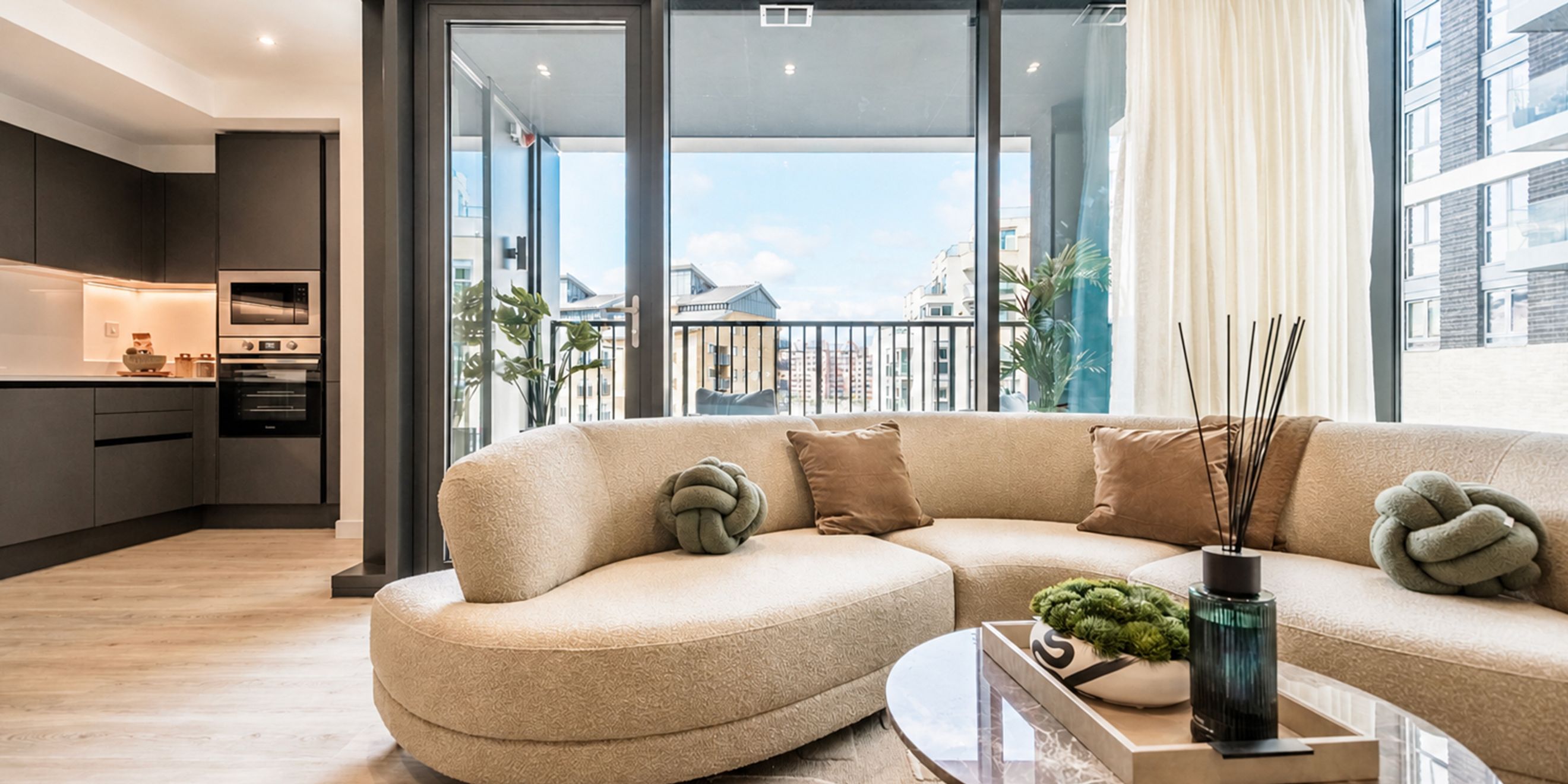 A modern living room and kitchen area with a curved sofa and balcony access.