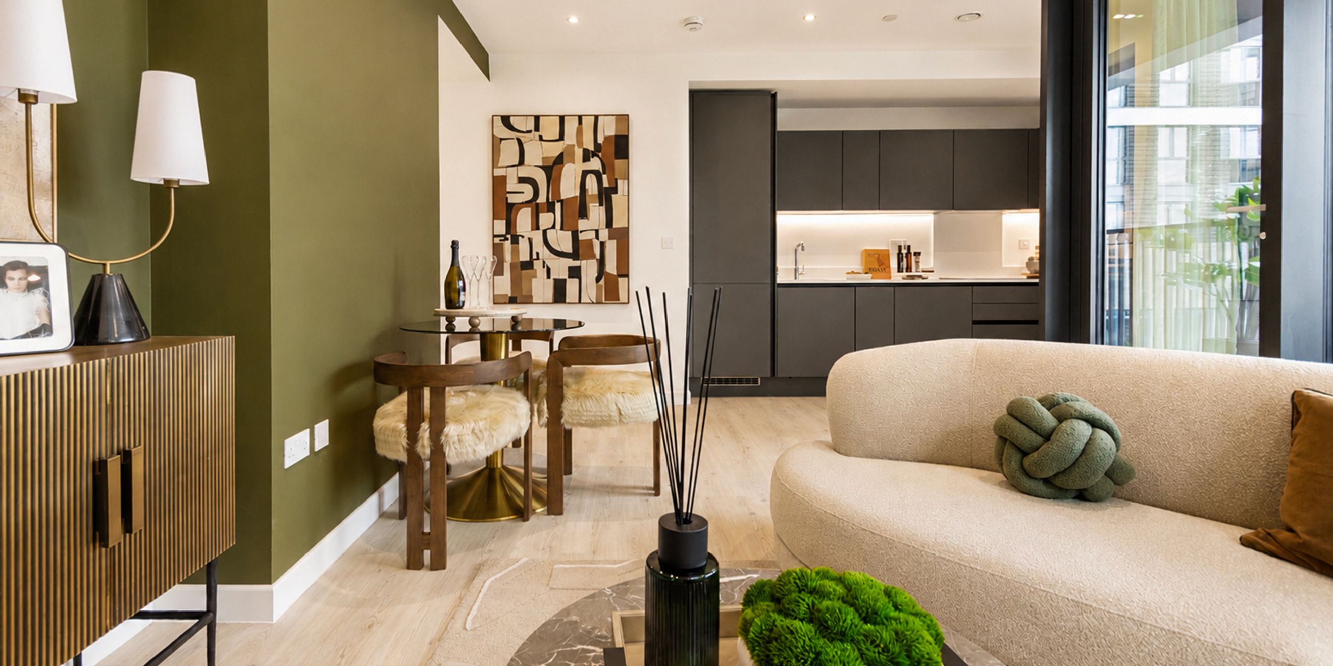 A living room and dining area with a sofa, dining table, chairs, and a kitchen in the background.