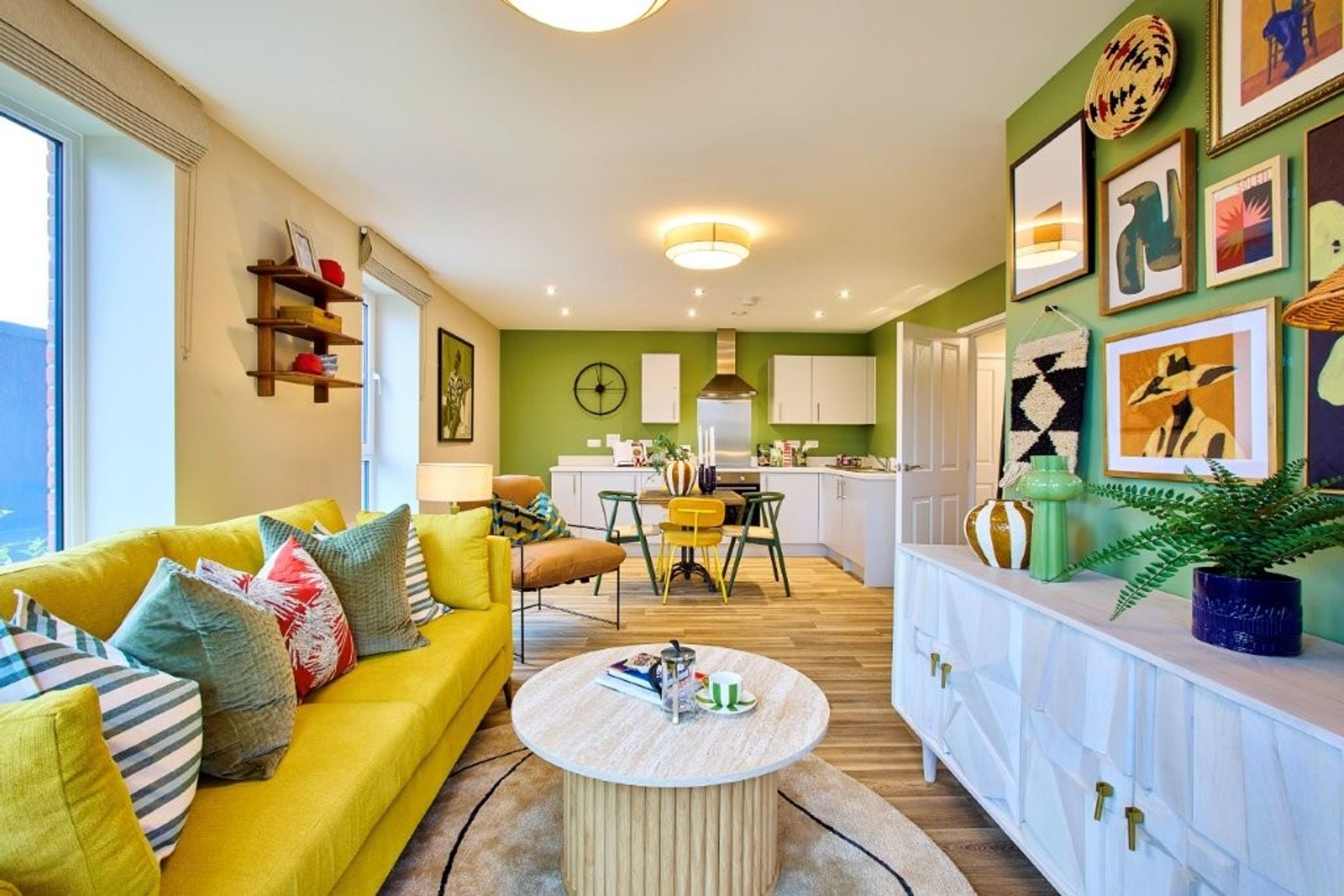 A living room and kitchen area with a yellow sofa, dining table, and white cabinets.