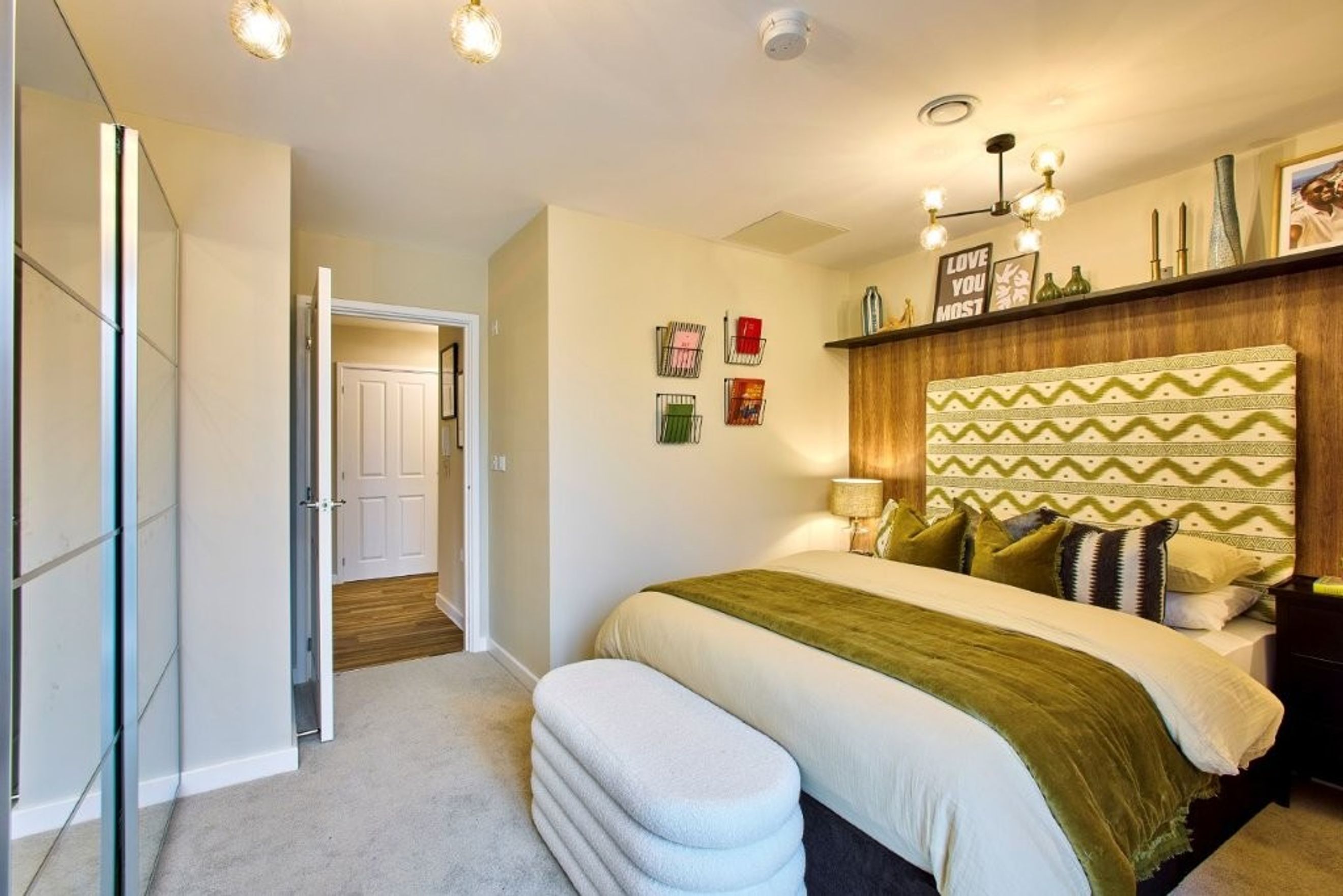 A bedroom with a bed, headboard, pillows, and a mirrored wardrobe.
