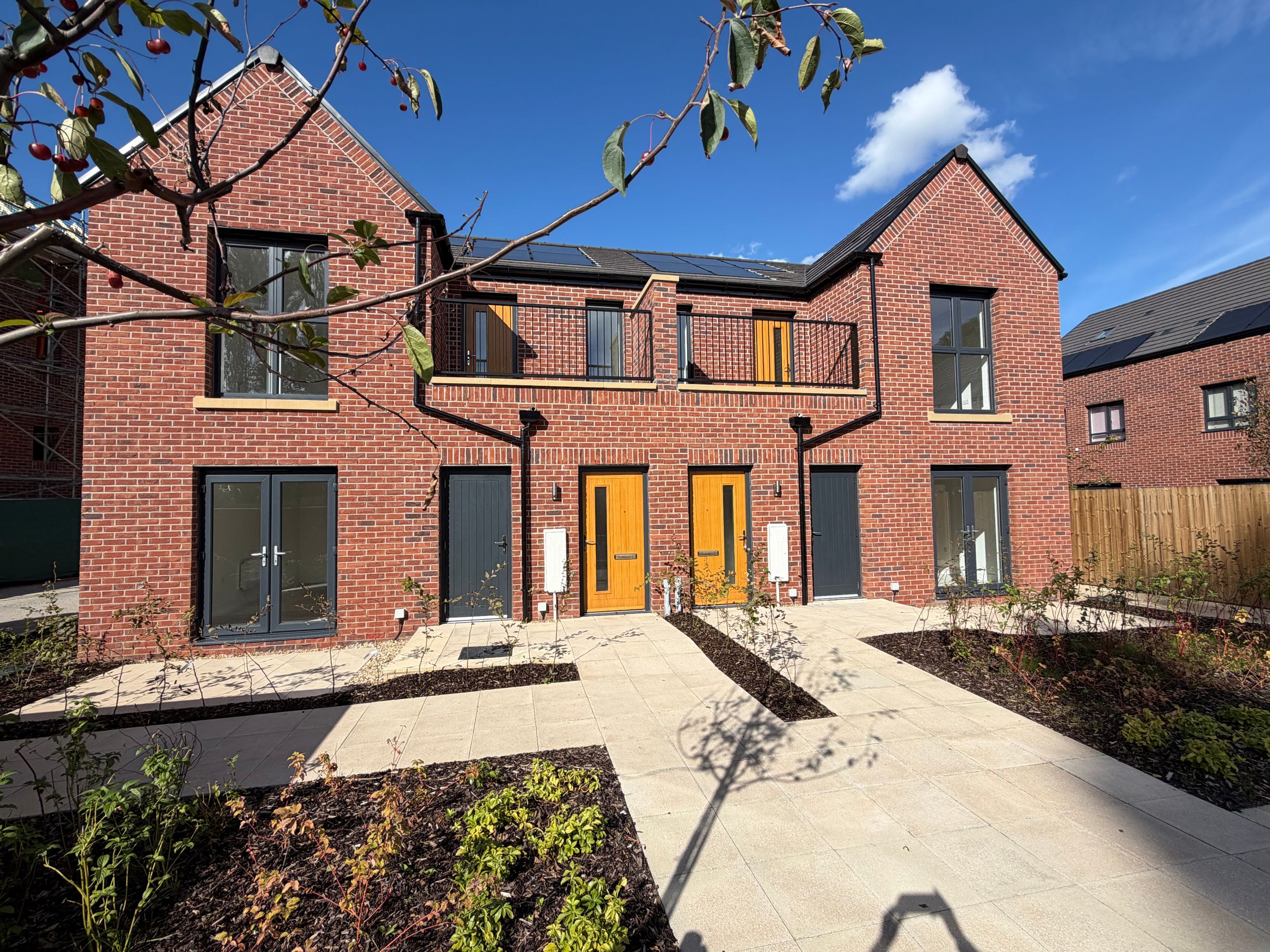 A row of modern brick houses with multiple doors and windows, balconies, and solar panels on the roof.