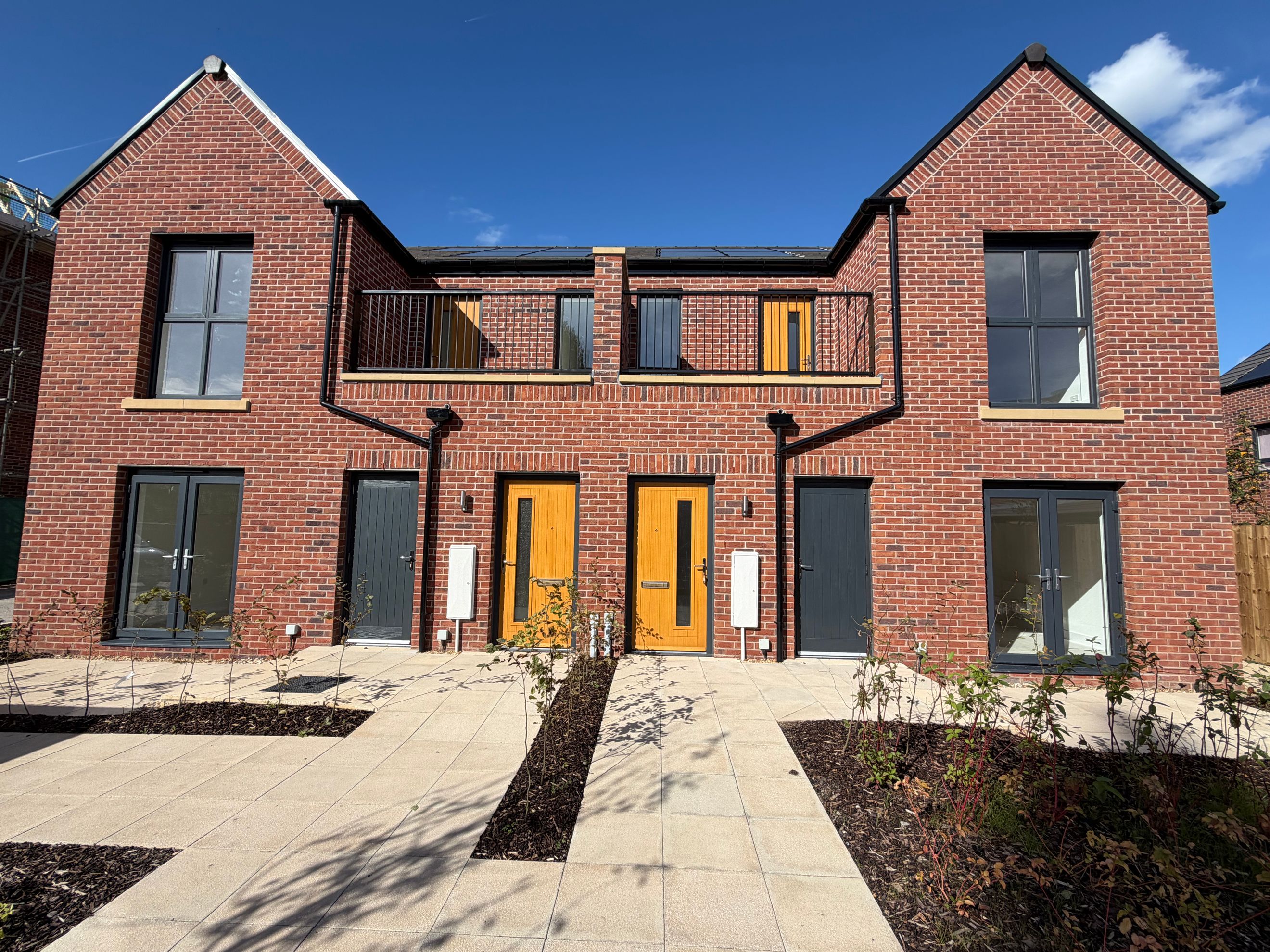 A row of new brick townhouses with balconies and multiple doors under a clear blue sky.