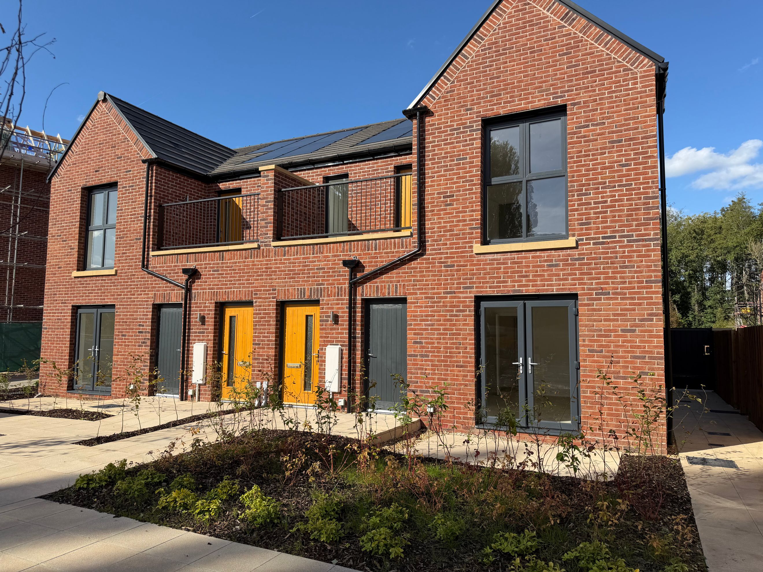 A row of modern red brick townhouses with balconies, solar panels, and landscaped gardens.