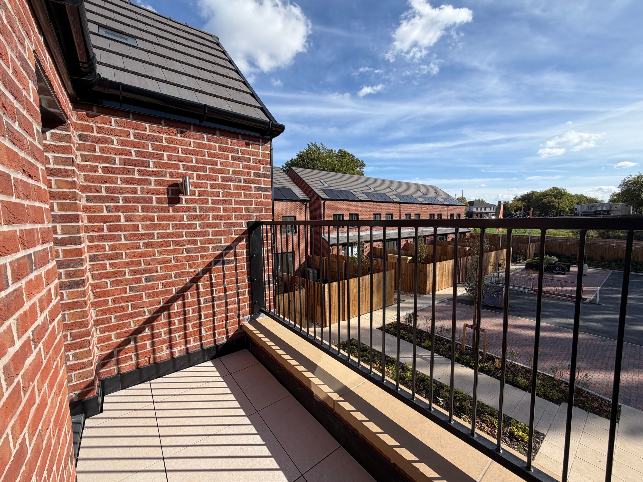 A balcony overlooking a street with brick houses and a blue sky with clouds.