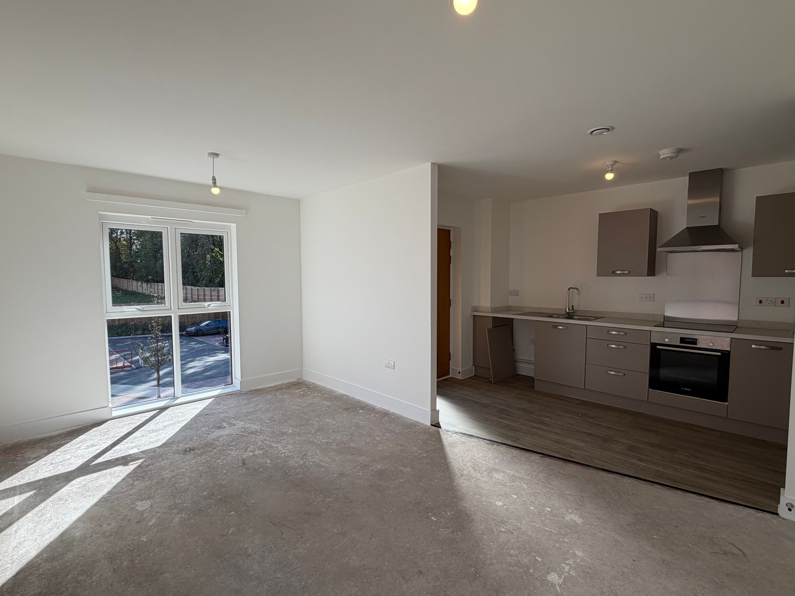 A living room and kitchen area in an unfurnished apartment.