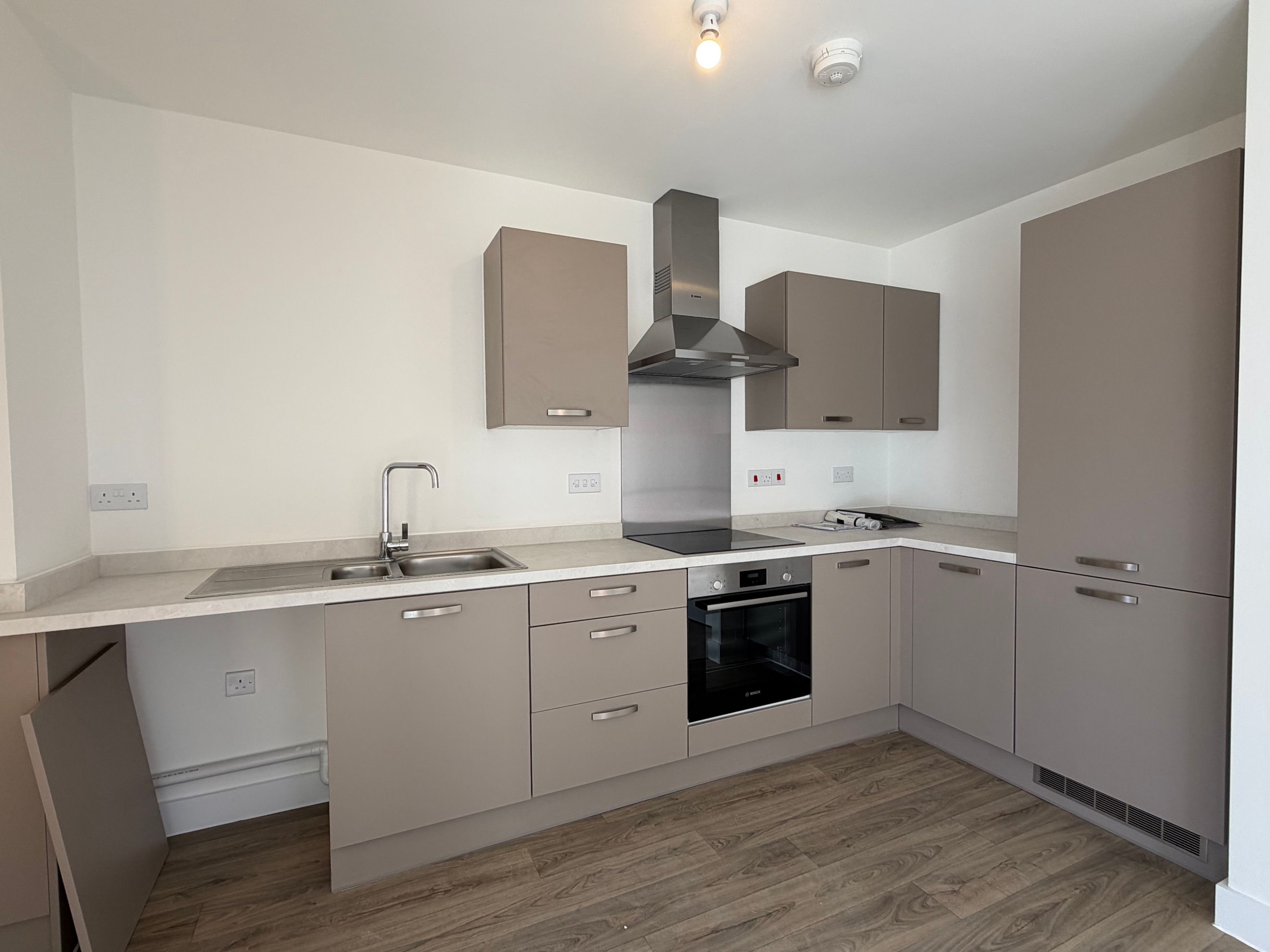 A modern kitchen with taupe cabinets, a sink, an oven, and an extractor hood.