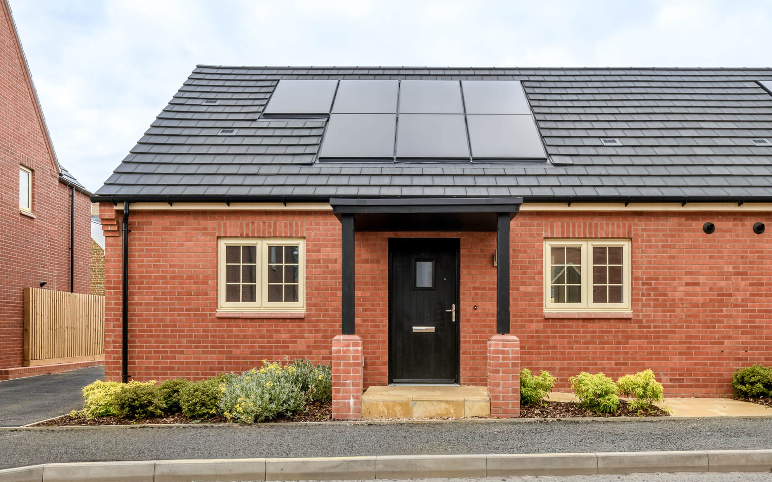 A brick house with a black front door, two windows, and solar panels on the roof.