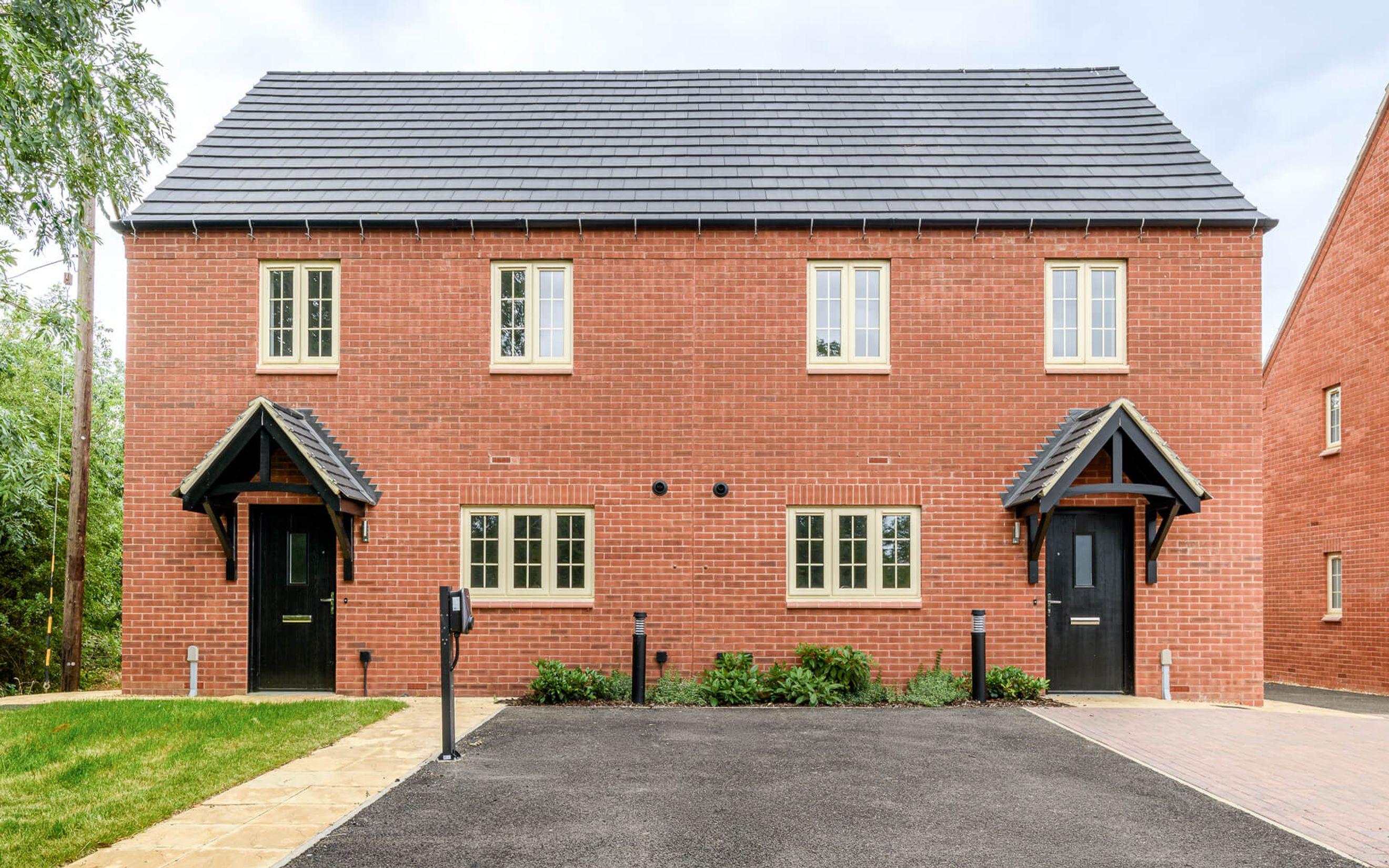 A pair of red brick semi-detached houses with black front doors and light cream windows.