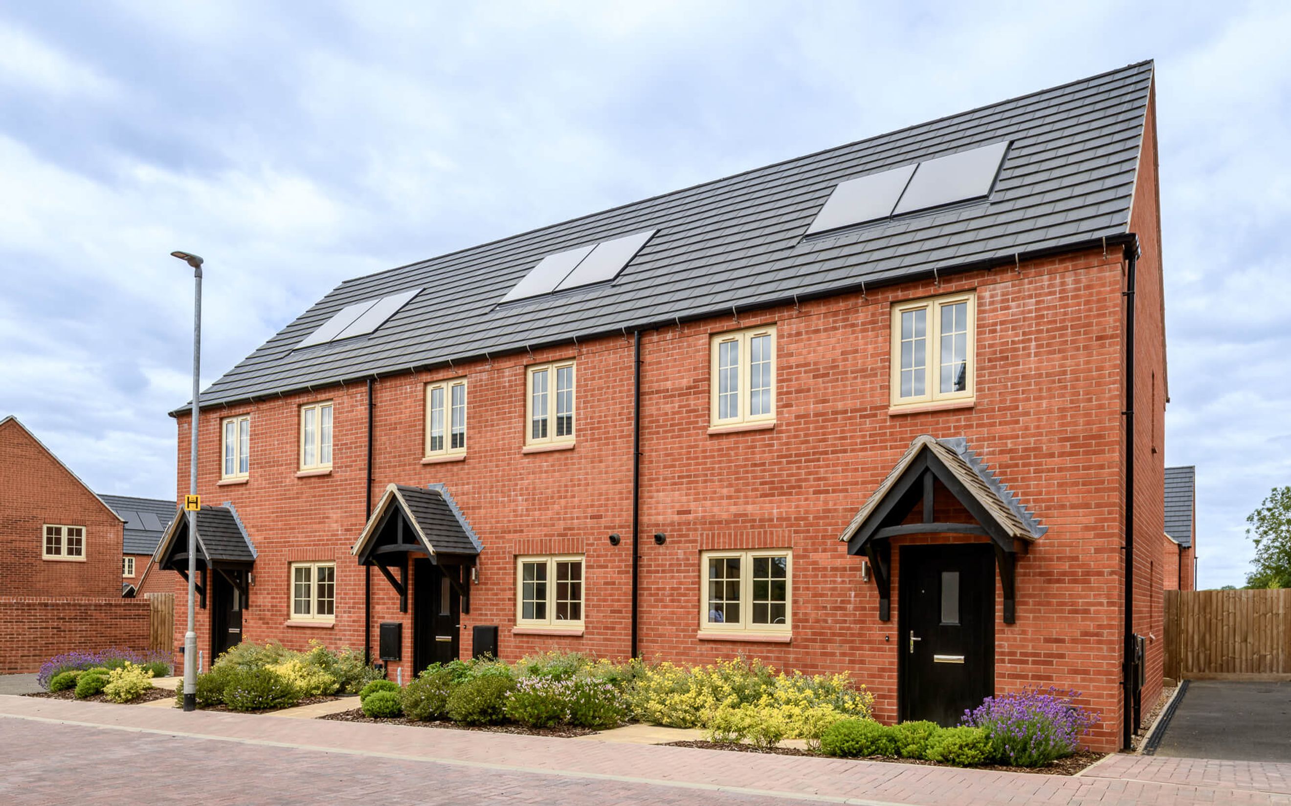 A row of modern red brick houses with grey tiled roofs and cream-framed windows.