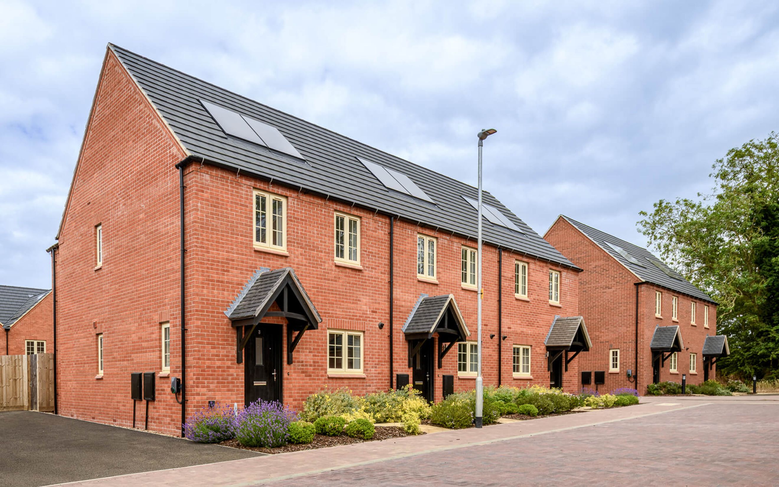 A row of modern red brick houses with grey tiled roofs and solar panels.