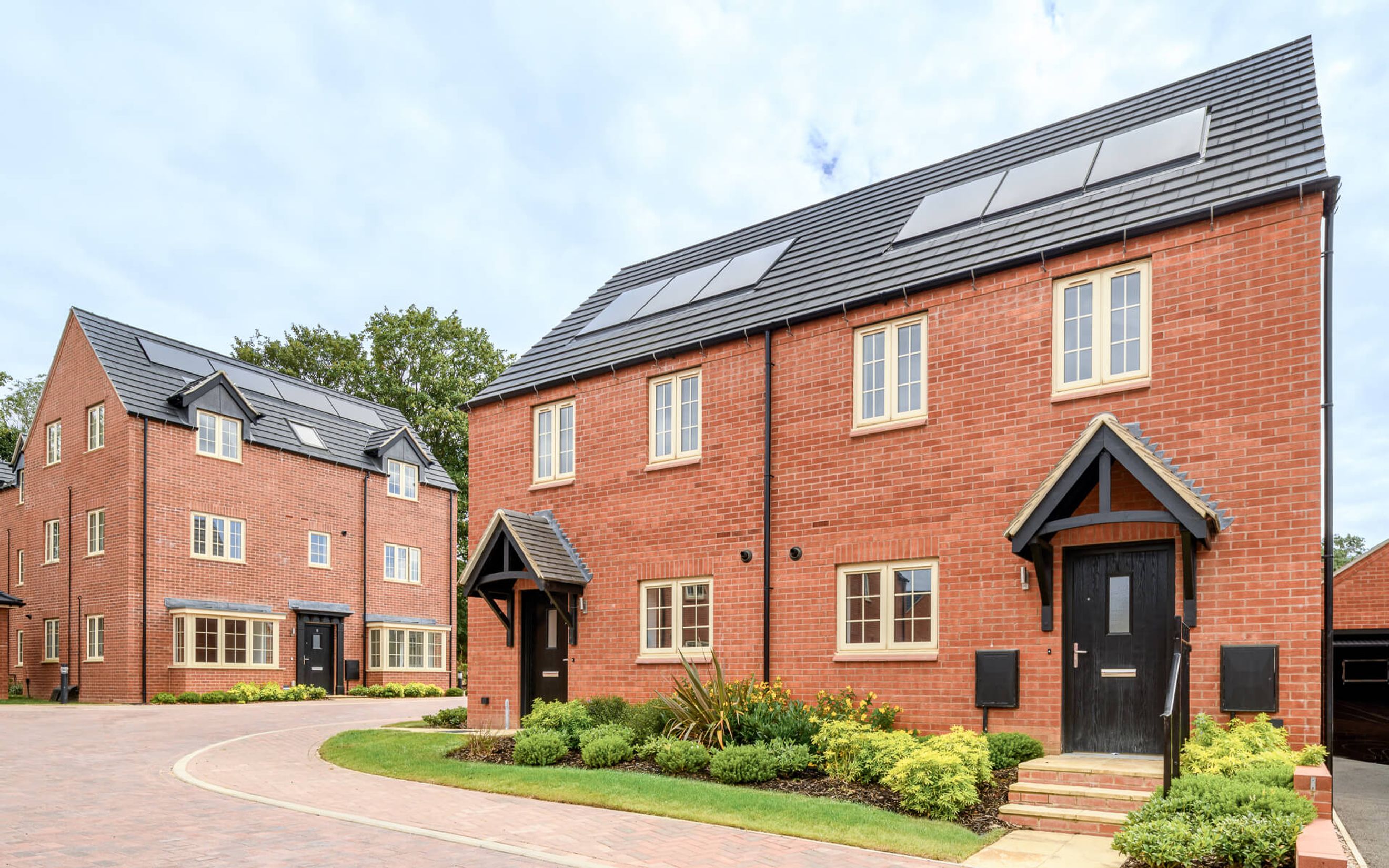 A row of modern red brick townhouses with dark roofs and light-colored windows.