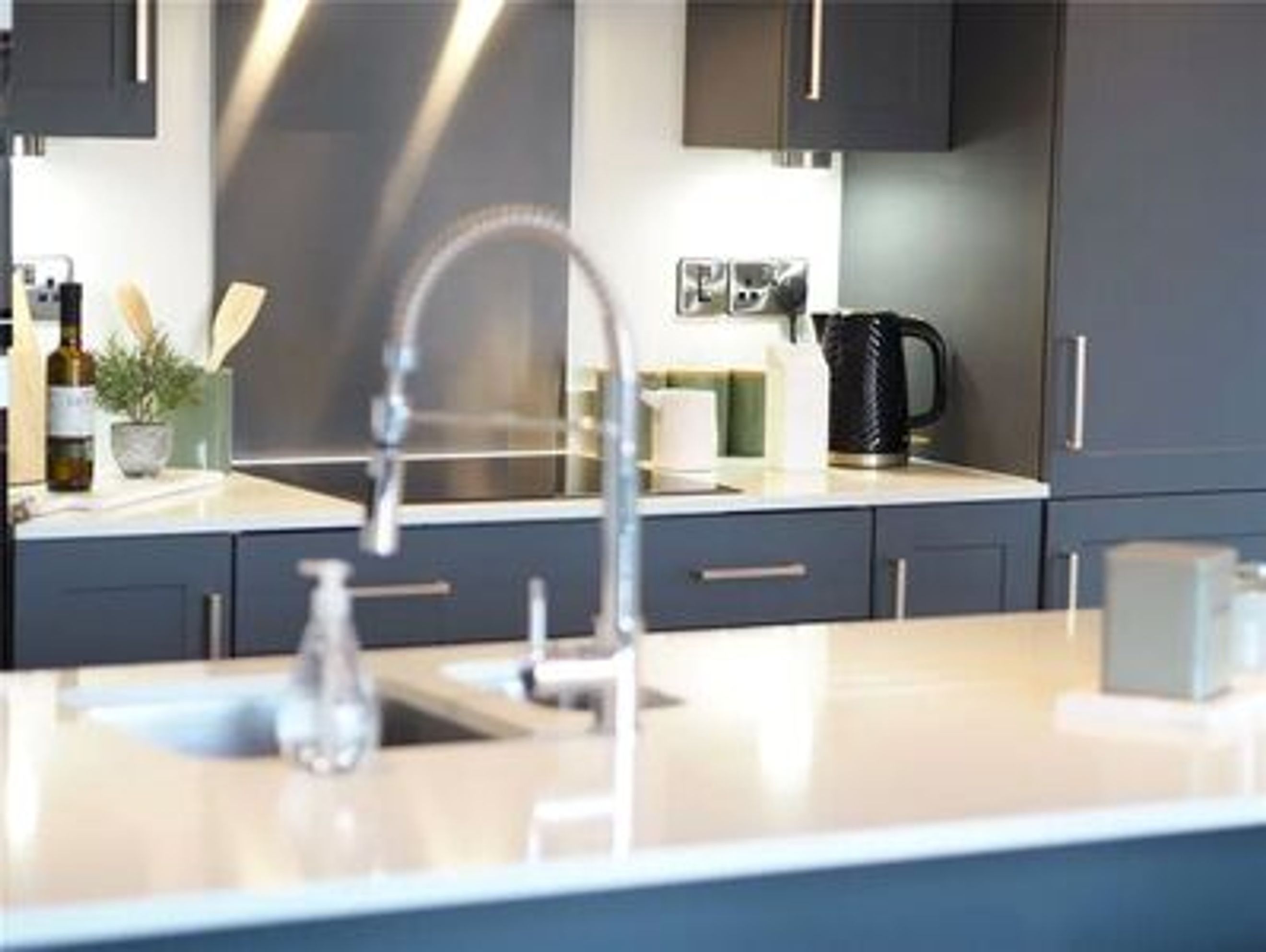 A kitchen with a sink, faucet, kettle, and cabinets.
