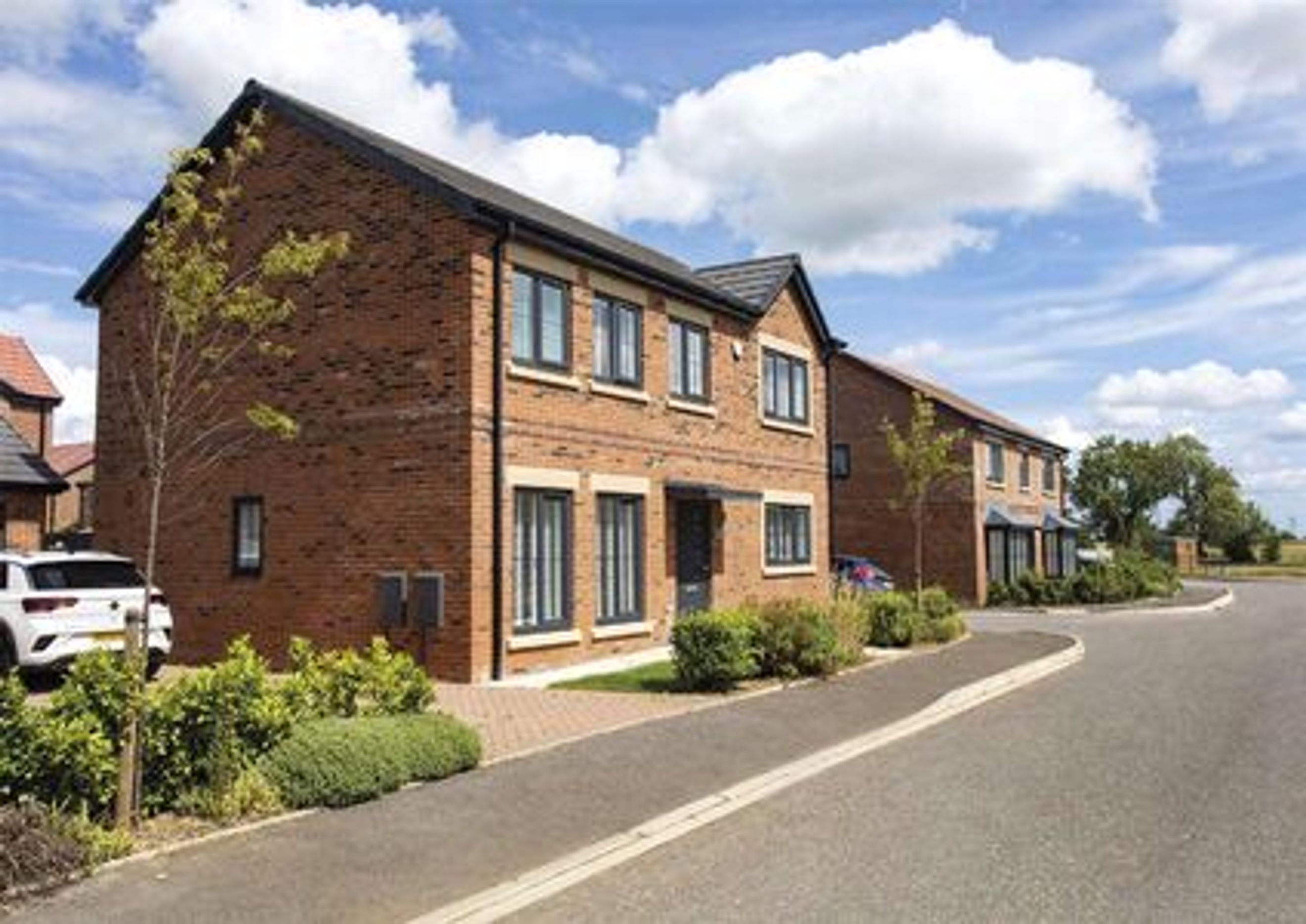 A row of modern brick houses with dark roofs and grey windows on a sunny day.