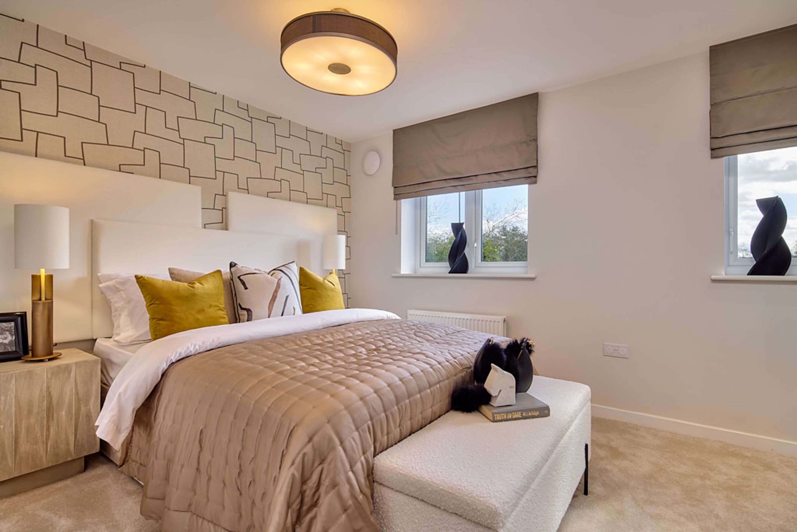 A bedroom with a bed, pillows, lamps, and windows.