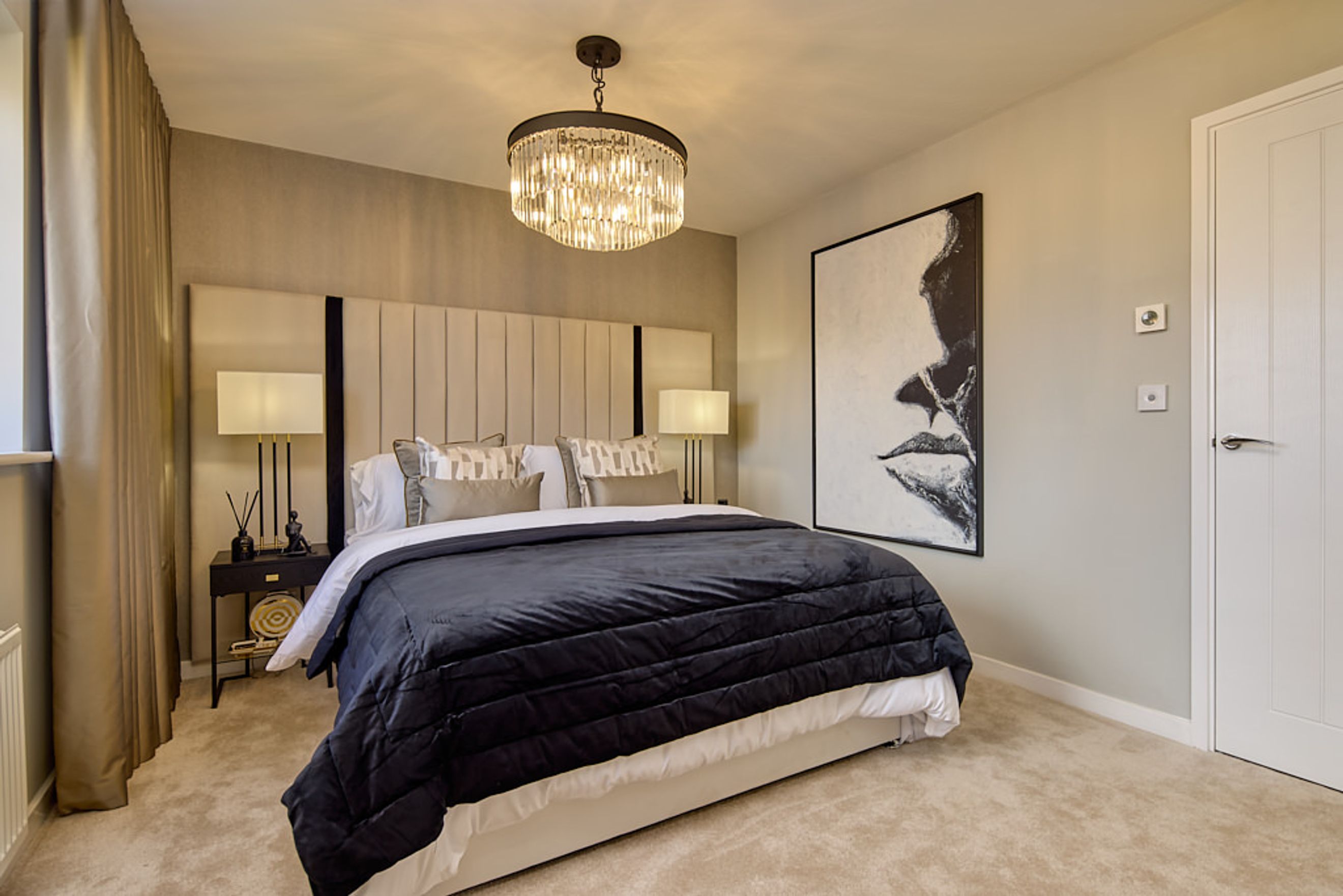 A bedroom with a bed, headboard, bedside tables, lamps, and a large artwork.