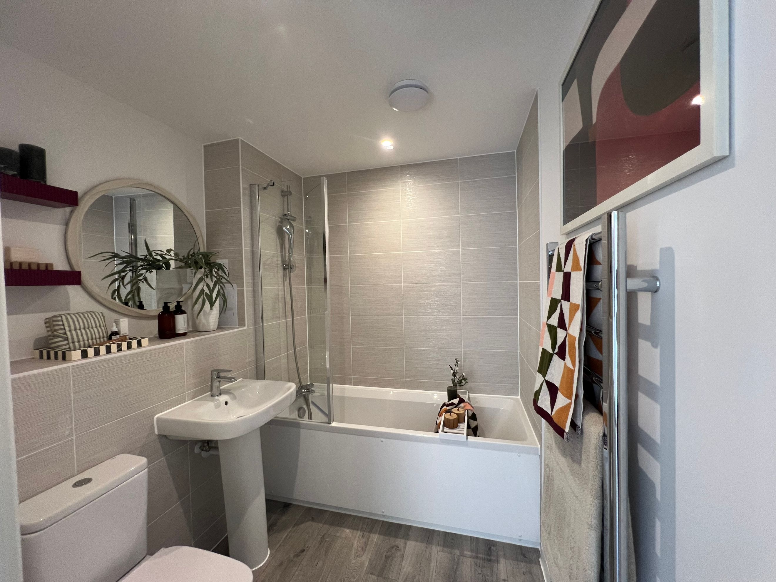 A bathroom with a bathtub, shower screen, sink, toilet, and decorative items.