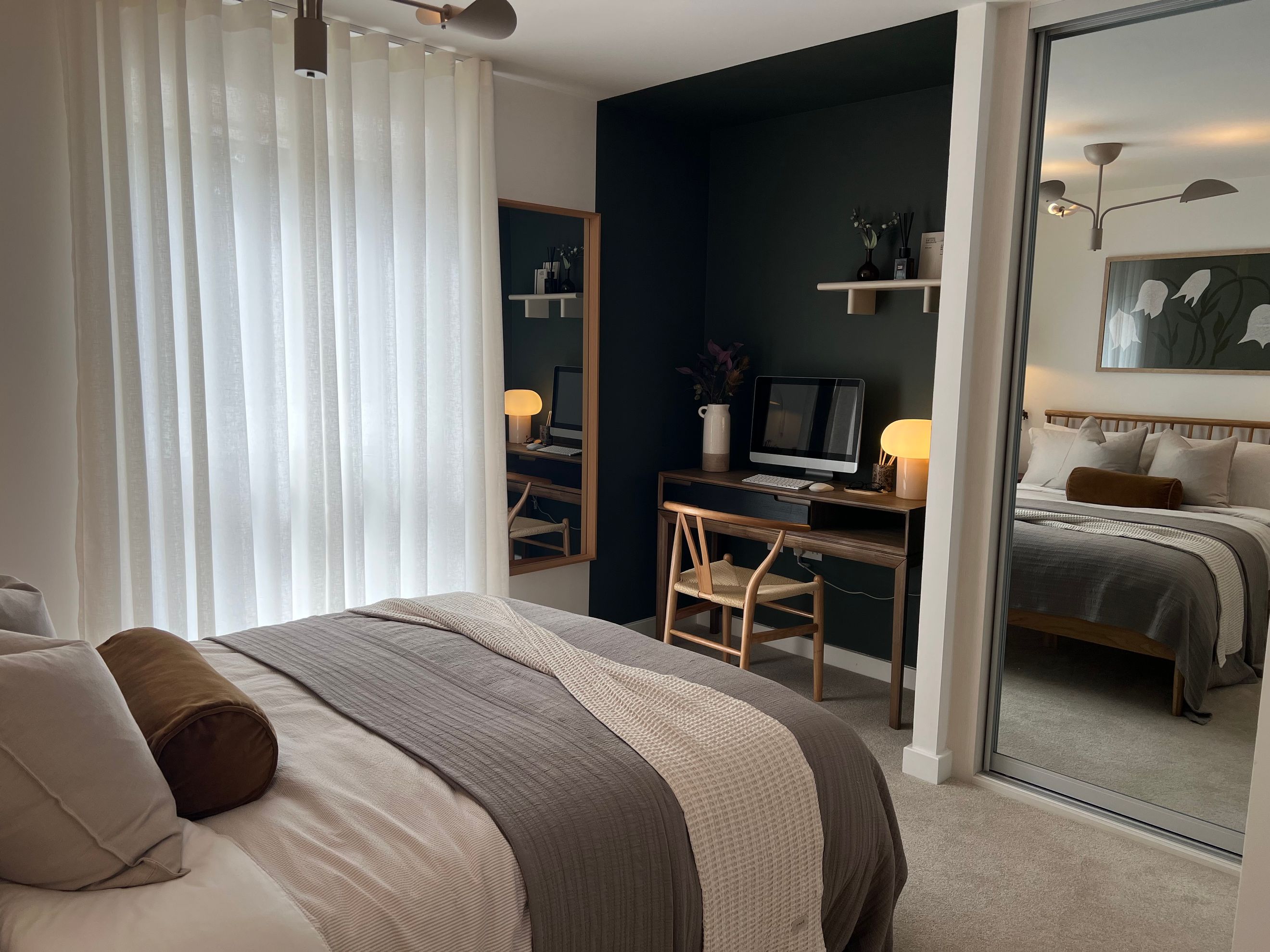 A bedroom with a bed, a desk, and a mirrored wardrobe.