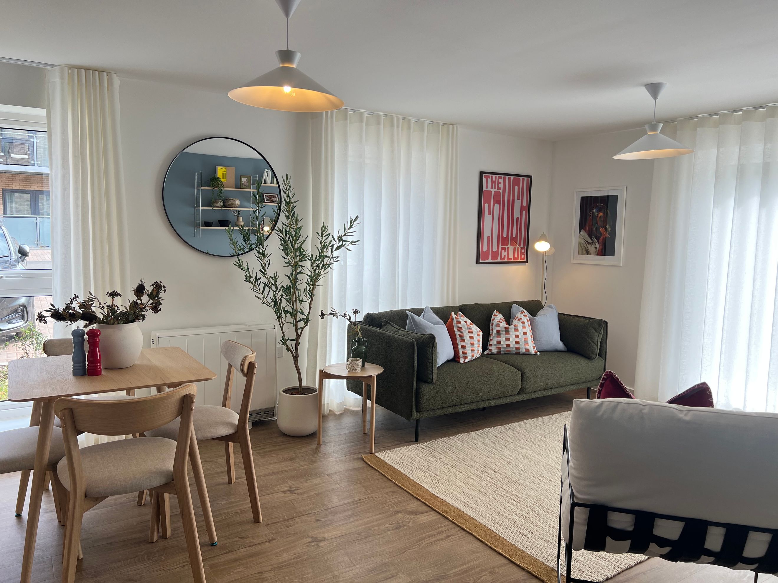 A living and dining area with a green sofa, dining table, chairs, and sheer curtains.