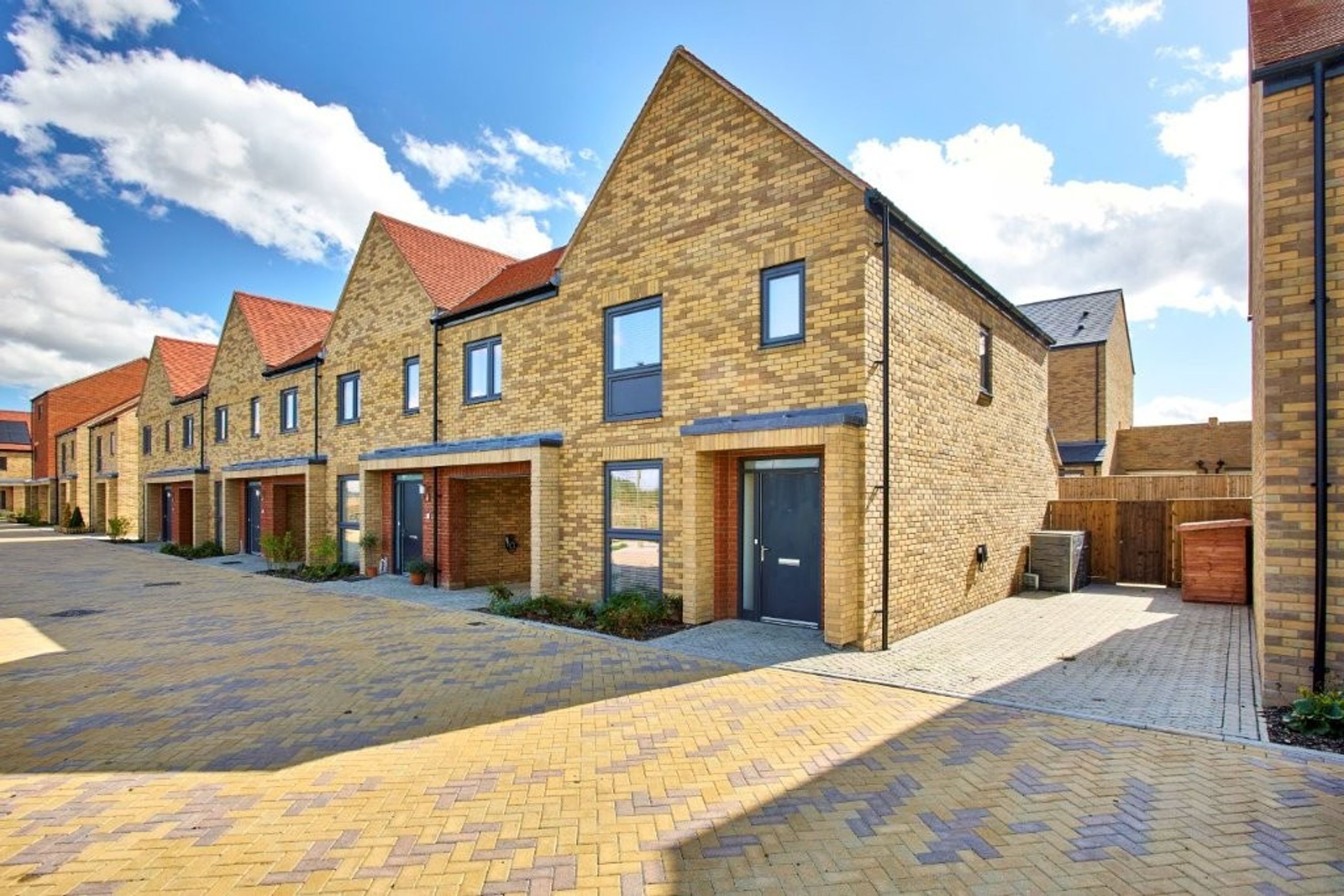 A row of modern brick townhouses with red tiled roofs and dark grey doors and windows.