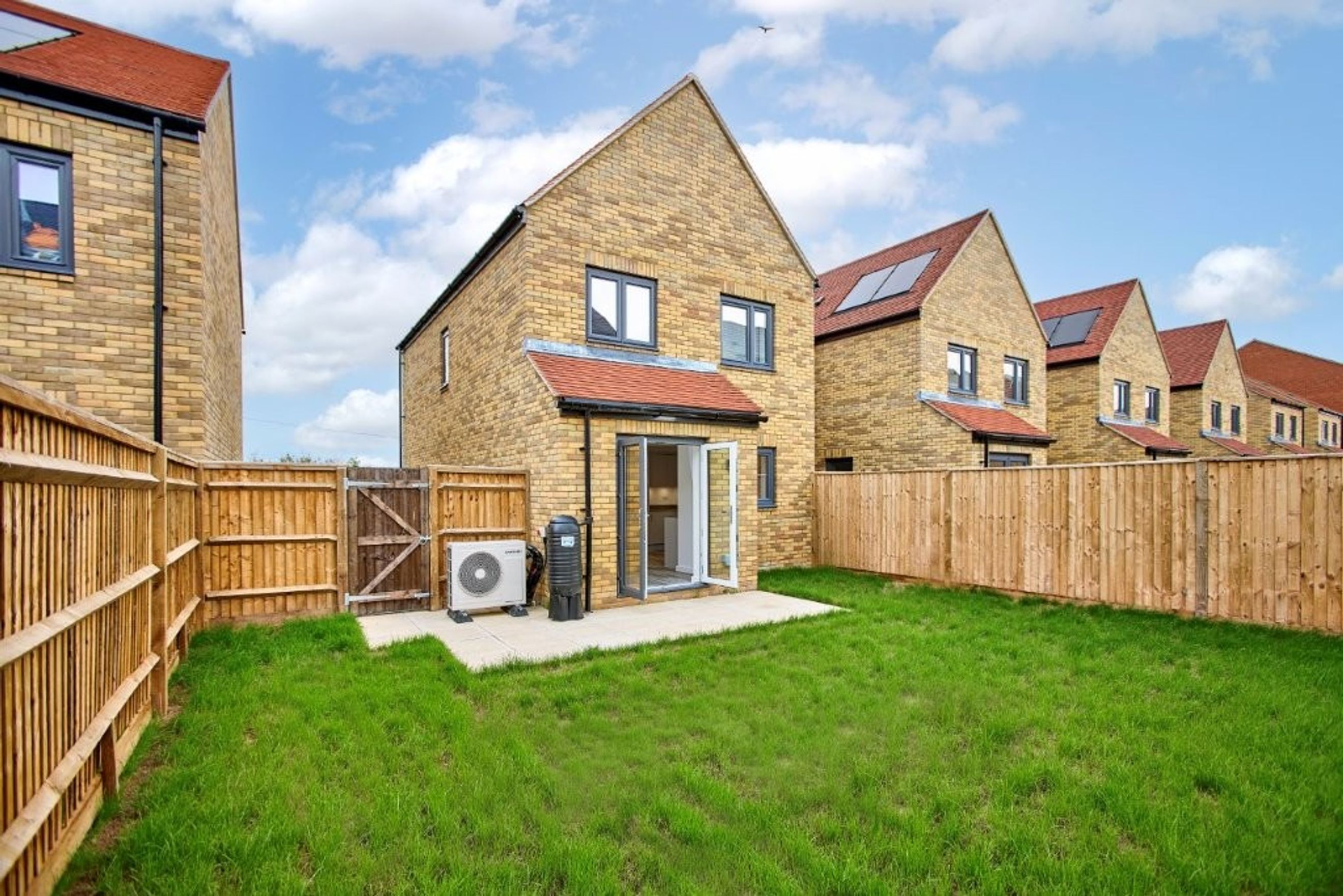 A backyard with a lawn, fence, and a house with double doors.