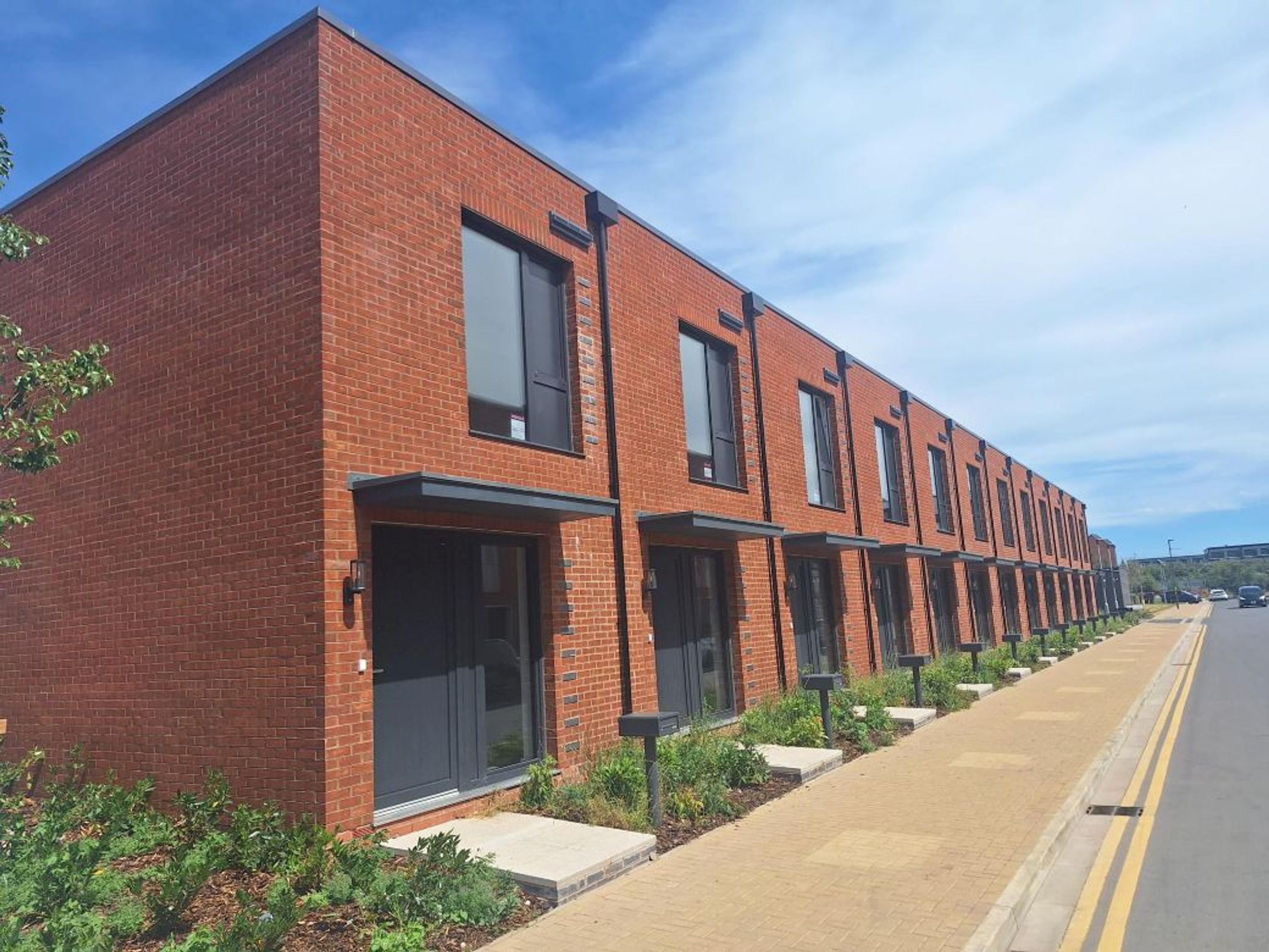 A row of modern brick townhouses with dark doors and windows, situated along a paved walkway.