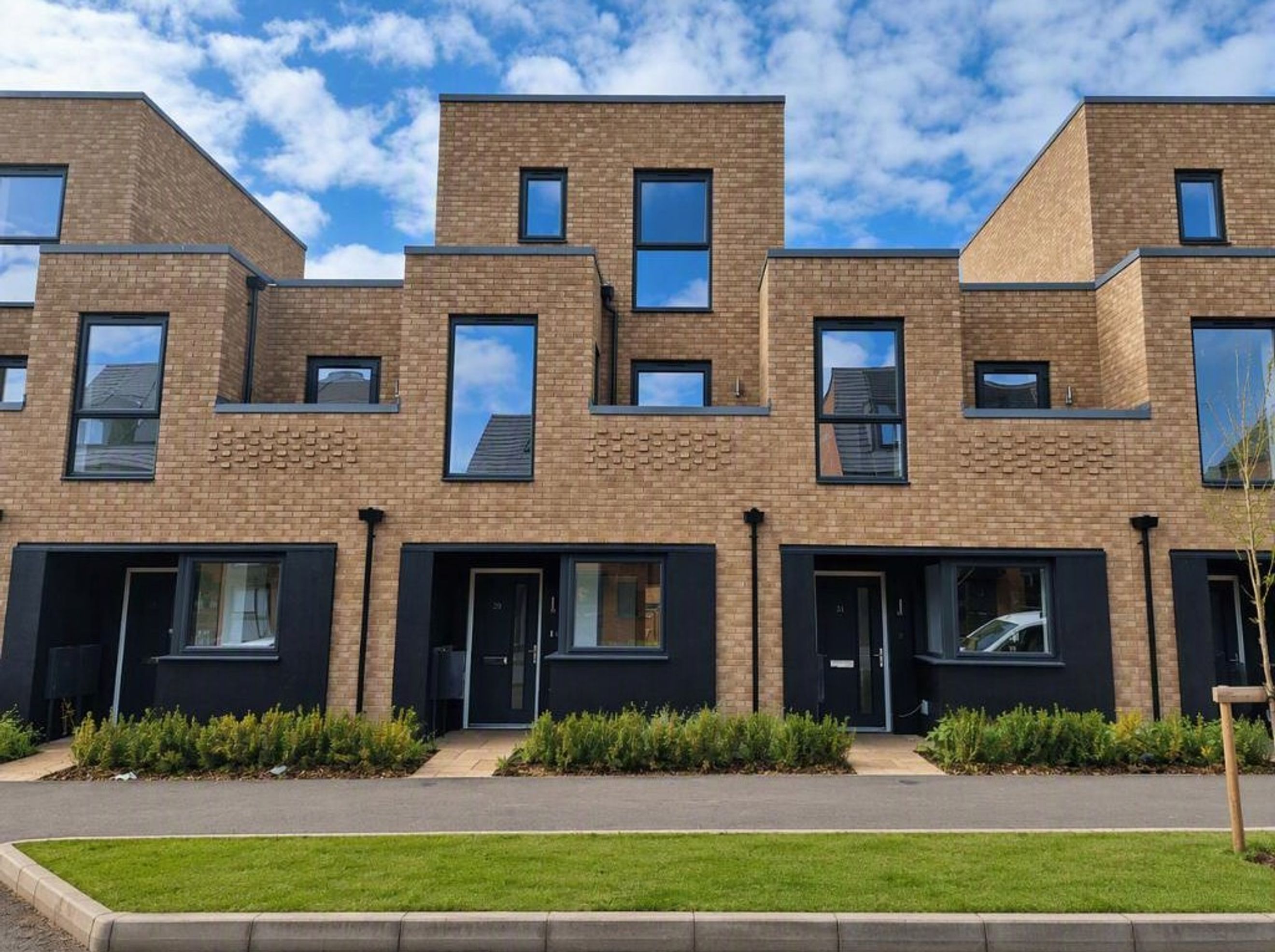 A row of modern brick townhouses with dark-framed windows and black entranceways.