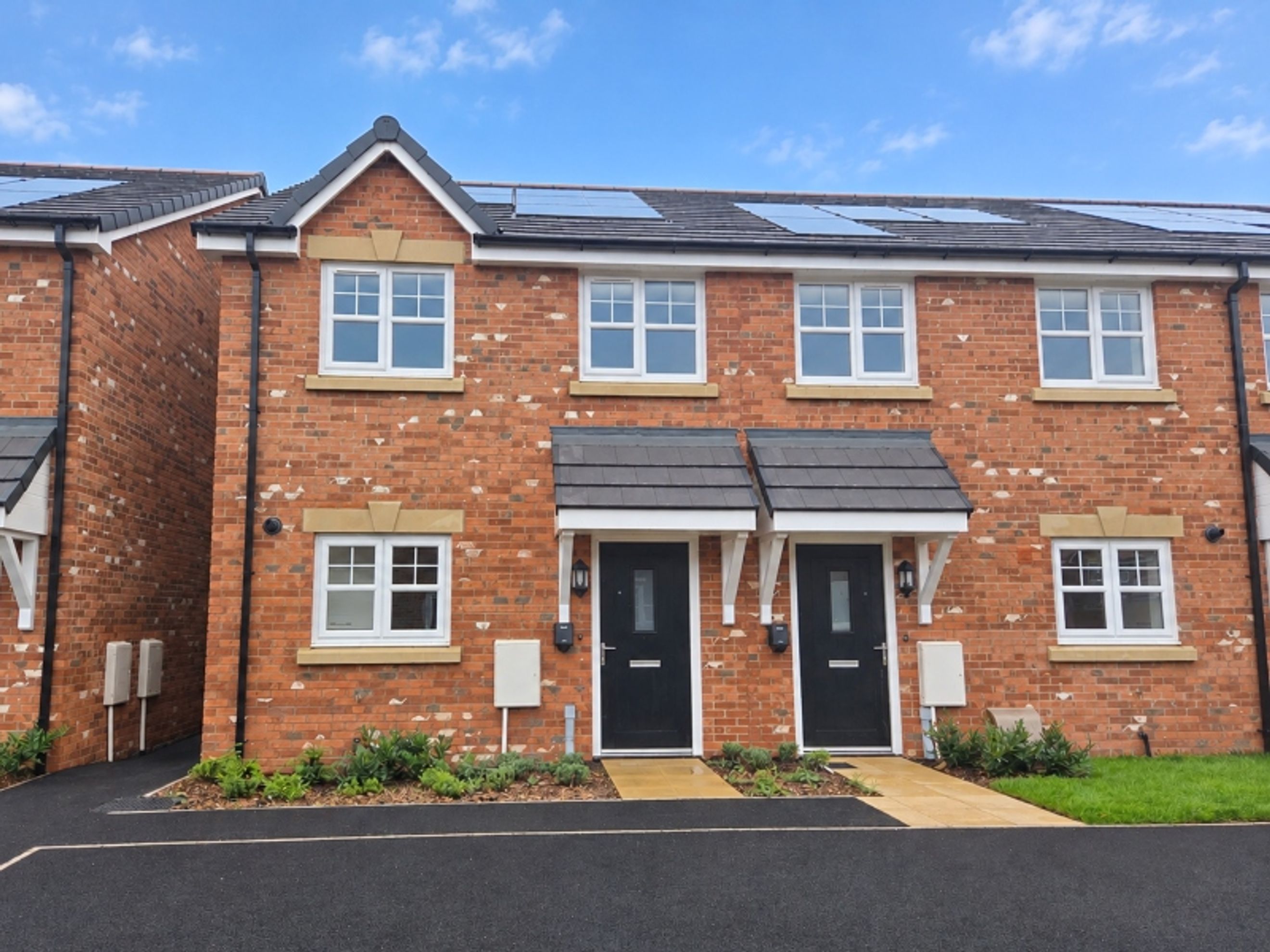 A row of modern red brick townhouses with white windows and black front doors under a blue sky.