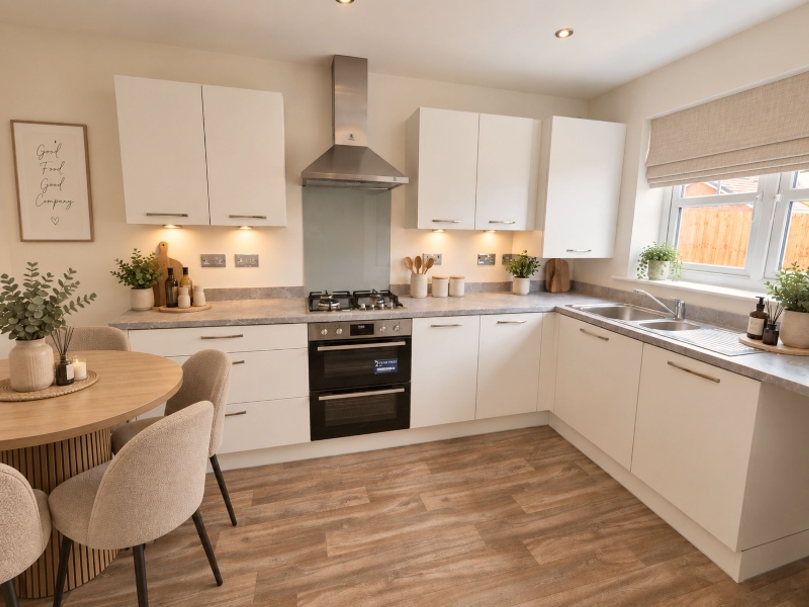 A modern kitchen with white cabinets, a stainless steel range hood, a double oven, and a round dining table.